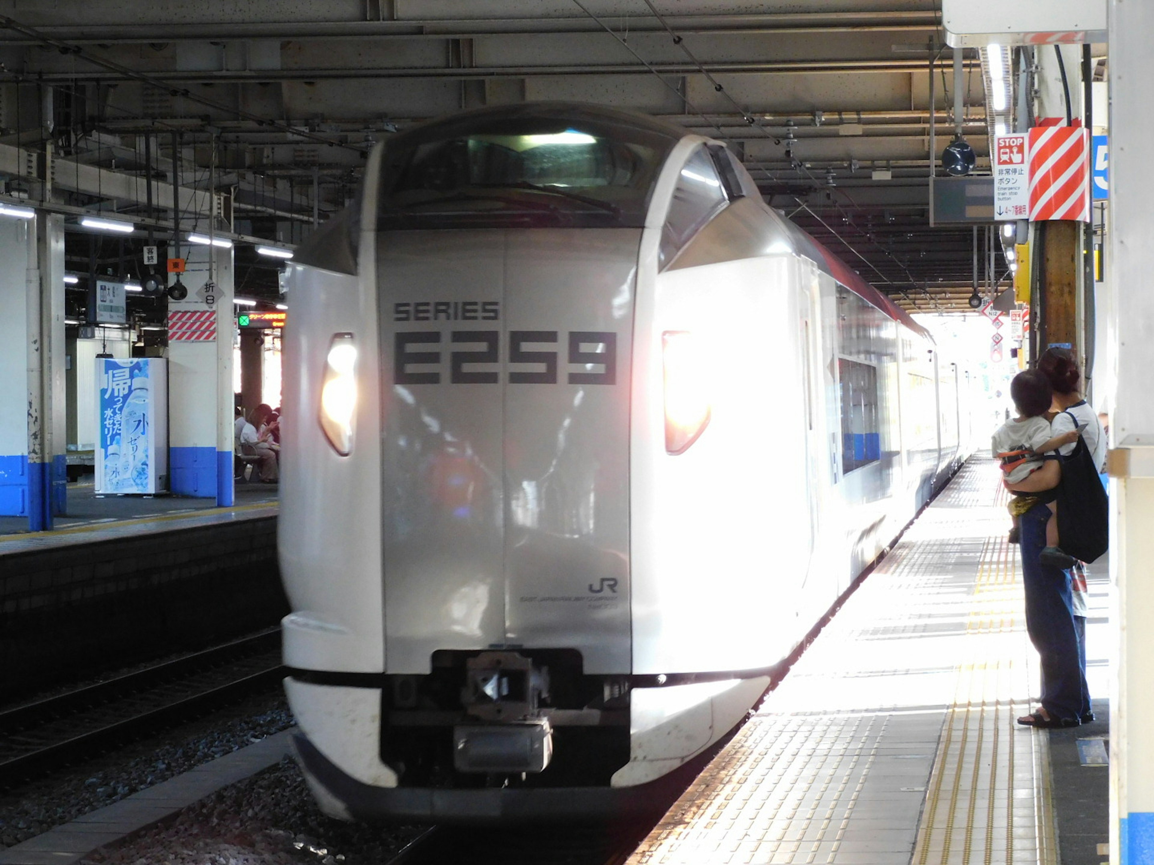 Sebuah kereta Shinkansen putih tiba di stasiun dengan penumpang menunggu