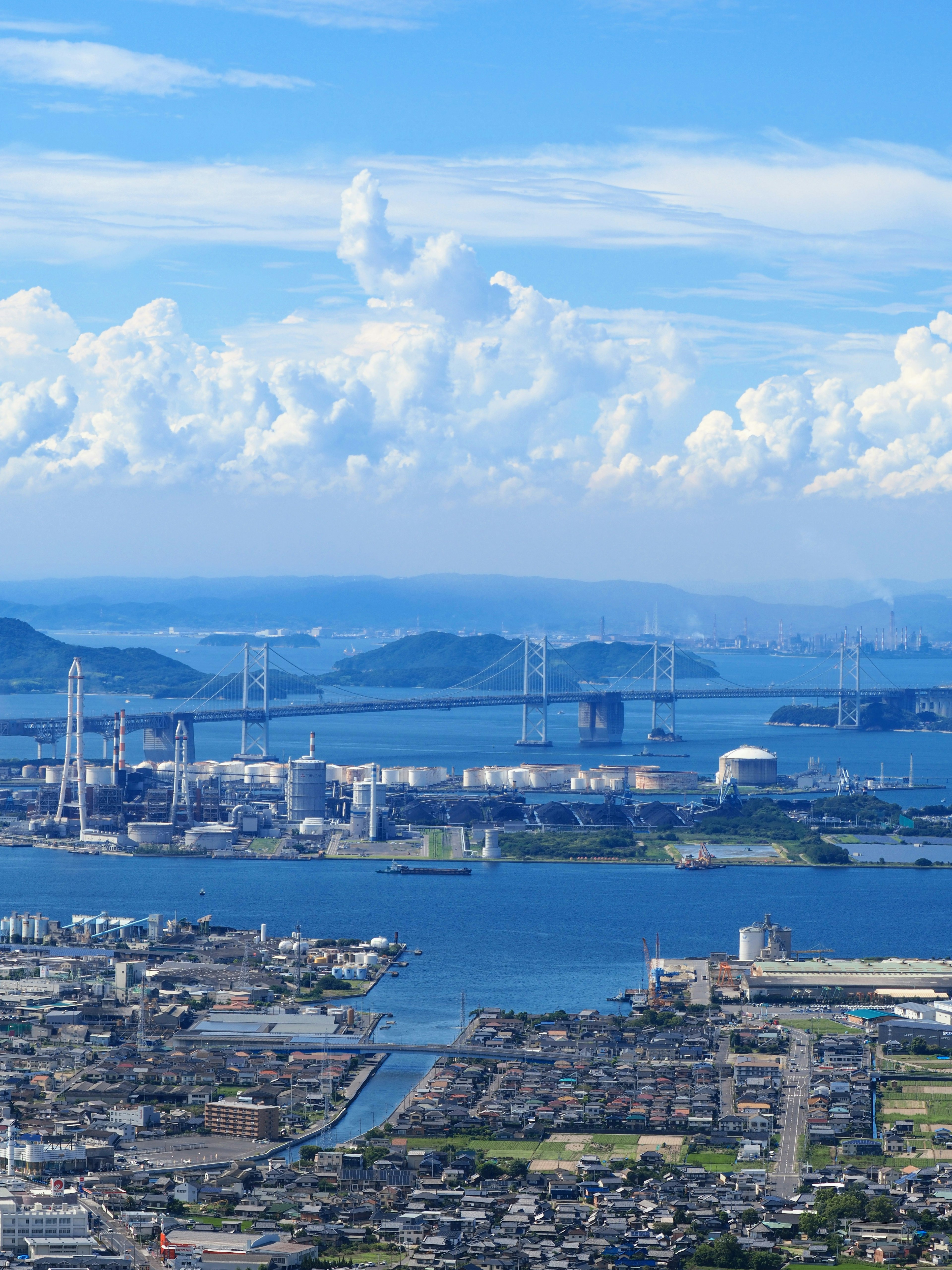 Vista costiera vibrante con cielo azzurro e nuvole bianche con un paesaggio urbano che include un porto e ponti