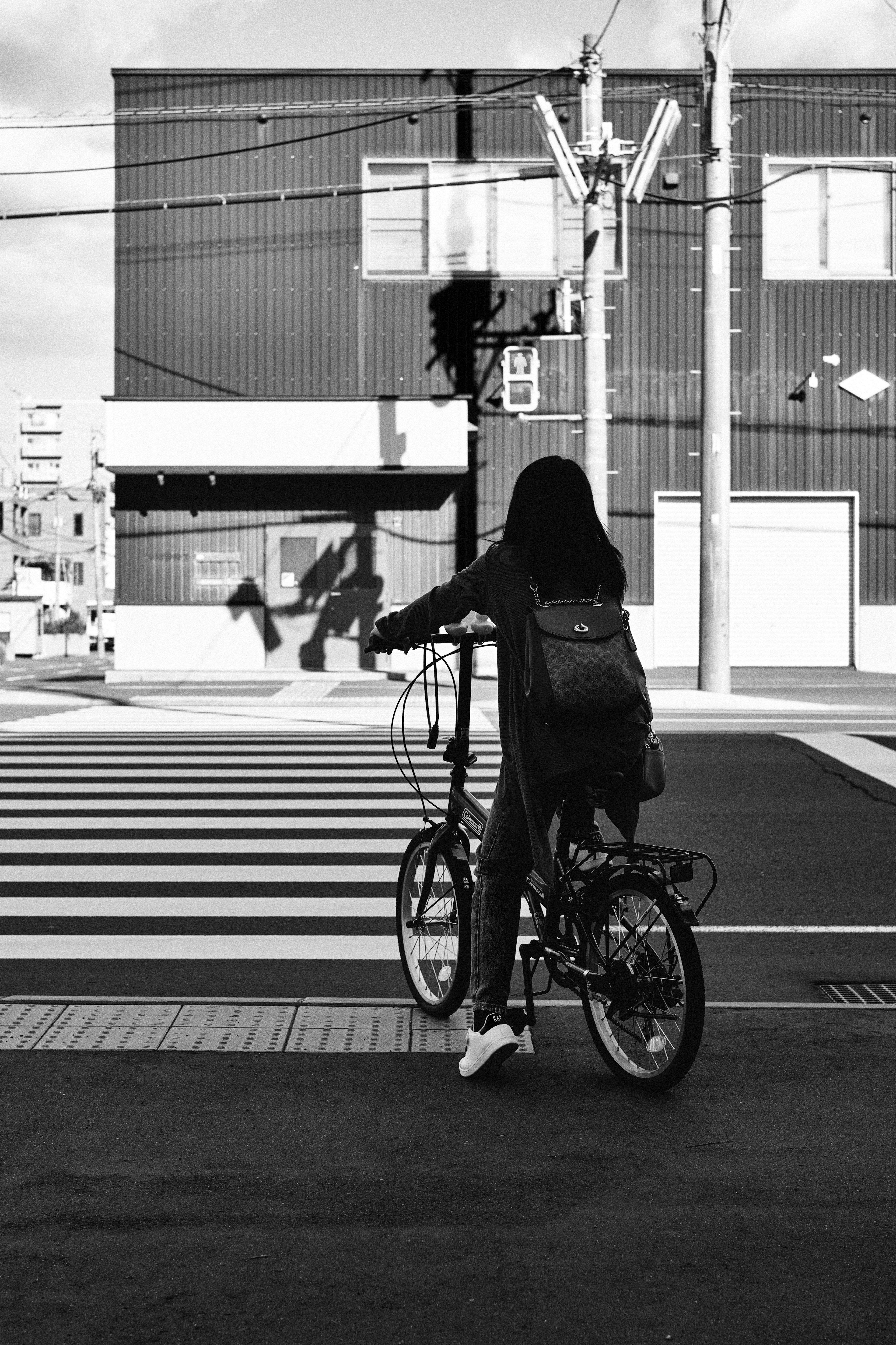 Seorang wanita di sepeda menunggu di zebra cross dengan lampu lalu lintas hitam putih