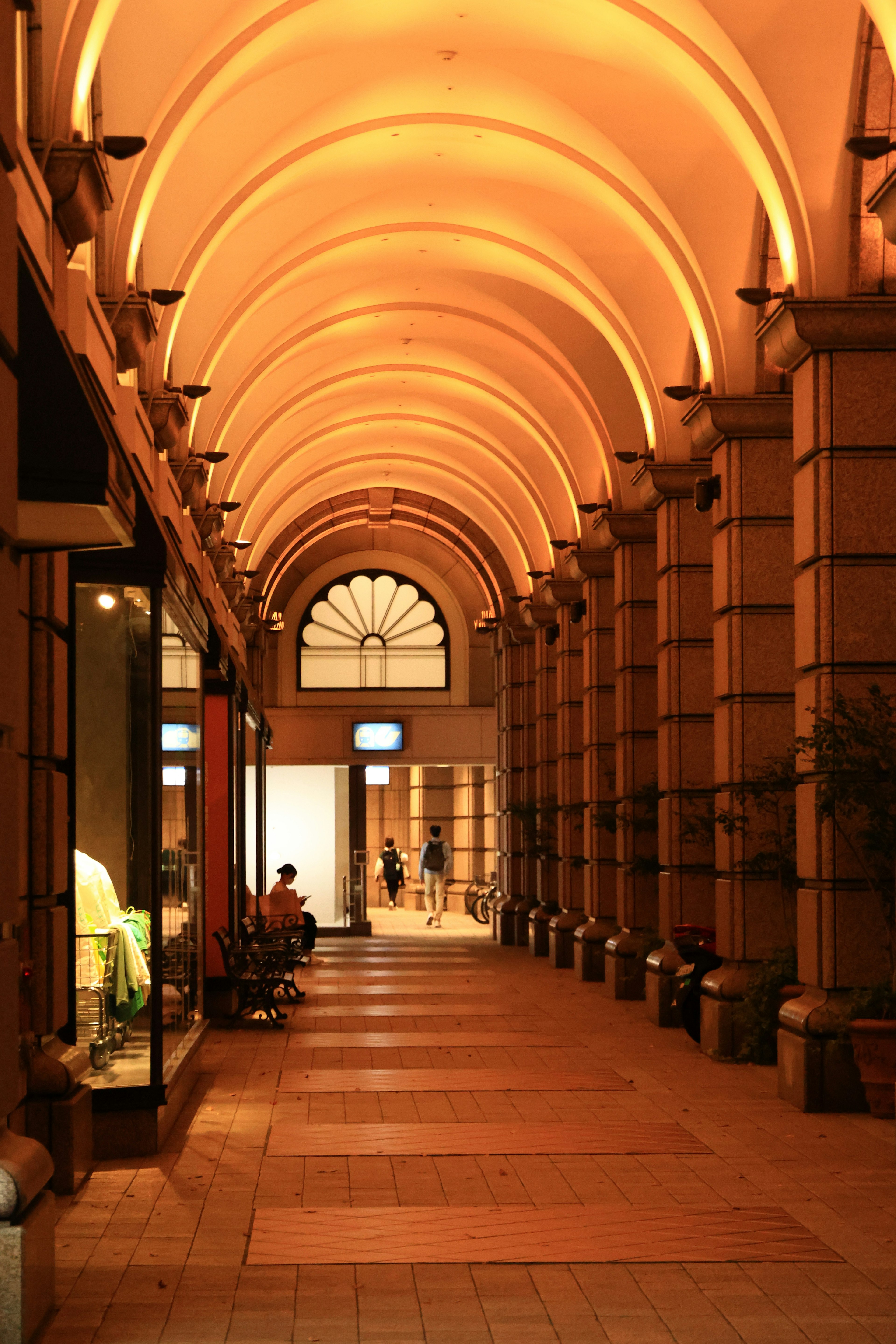 Photo of a bright corridor with arched ceilings featuring shop windows and warm lighting