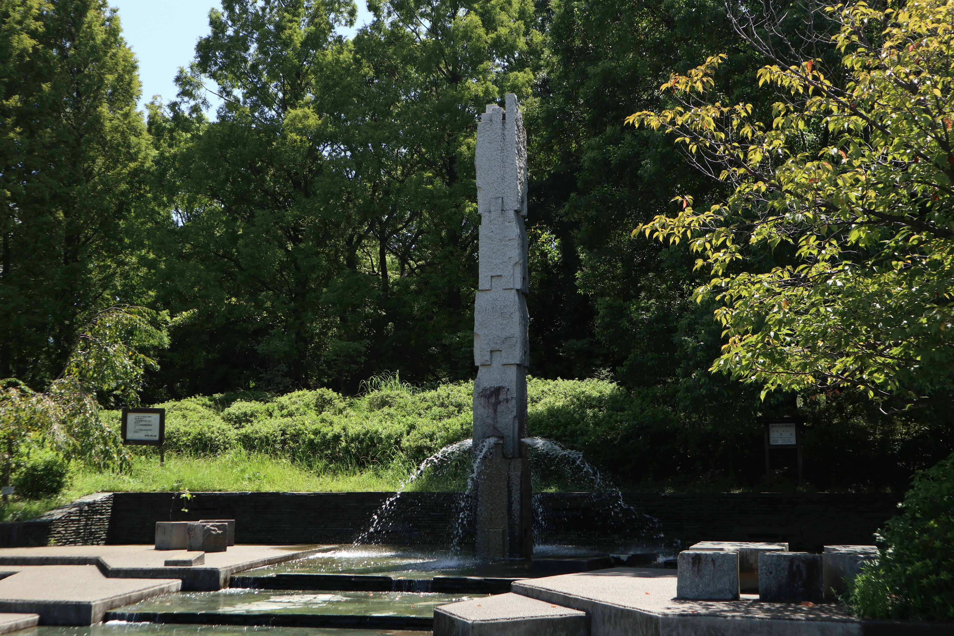 Stone sculpture and fountain in a park surrounded by green trees