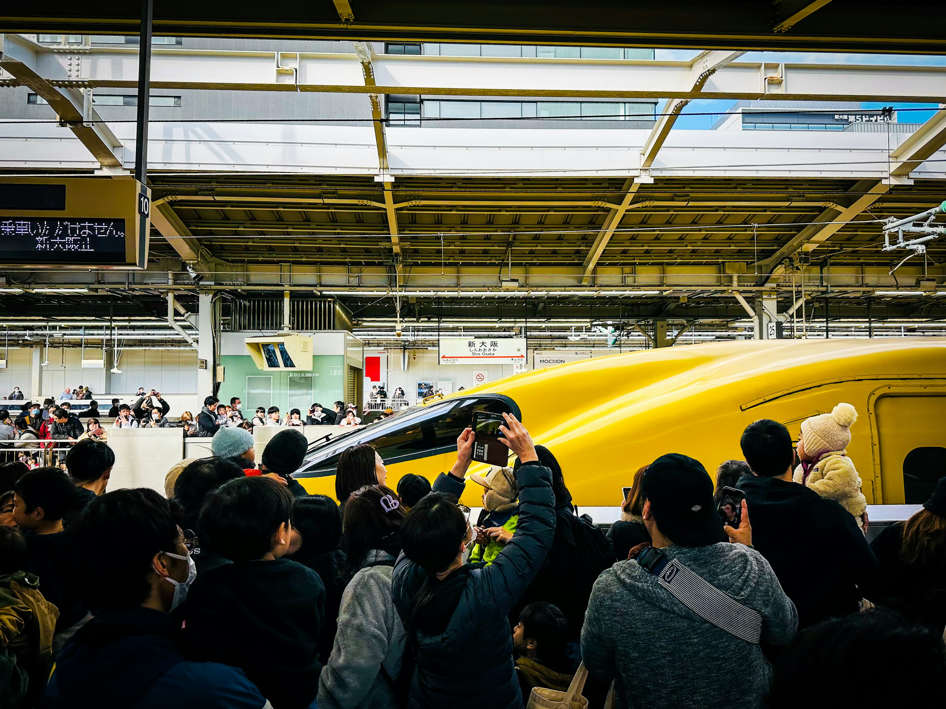 Crowd gathered around a yellow Shinkansen train at a station