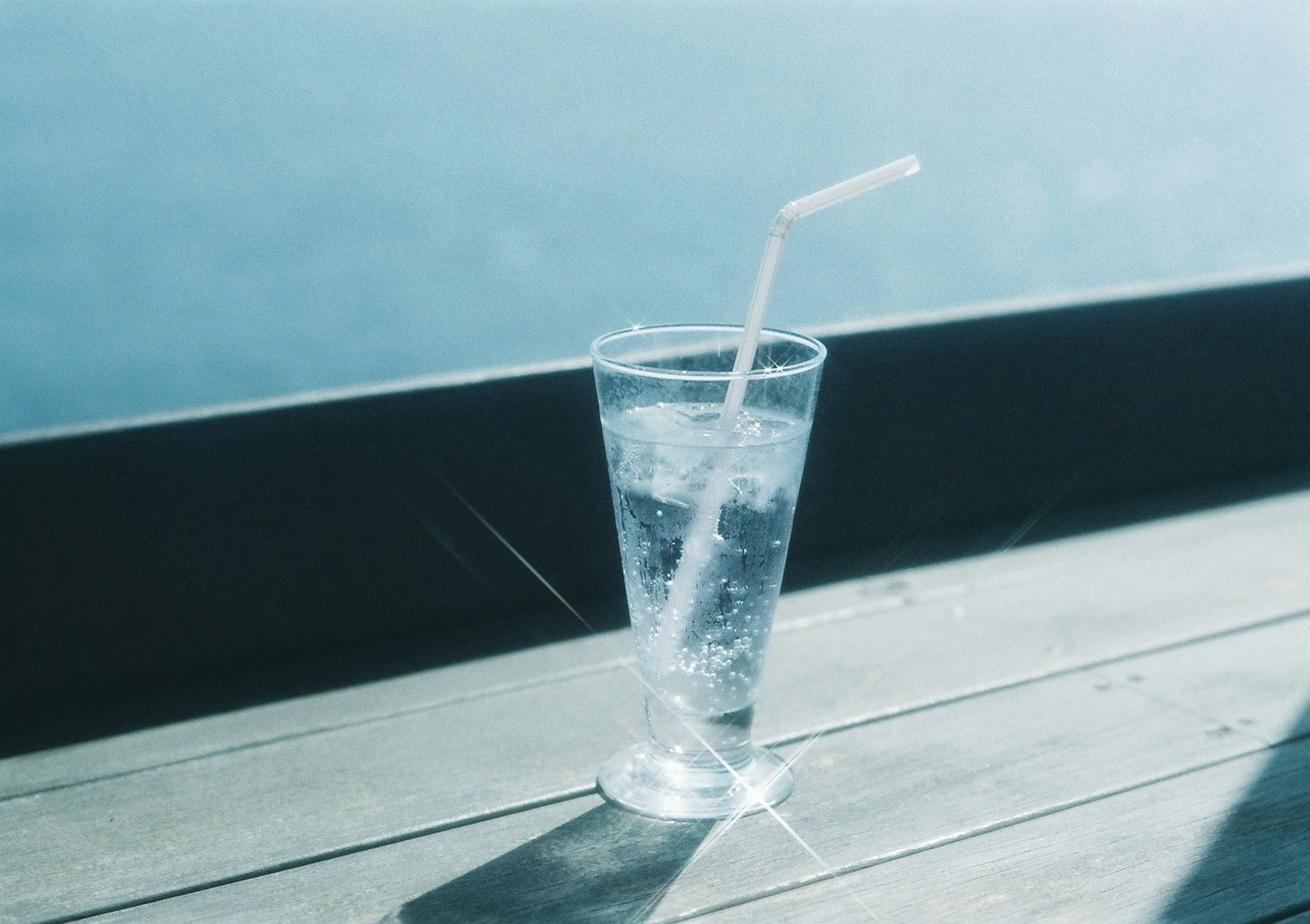 Un vaso de agua con una pajilla que refleja la luz sobre una superficie de madera