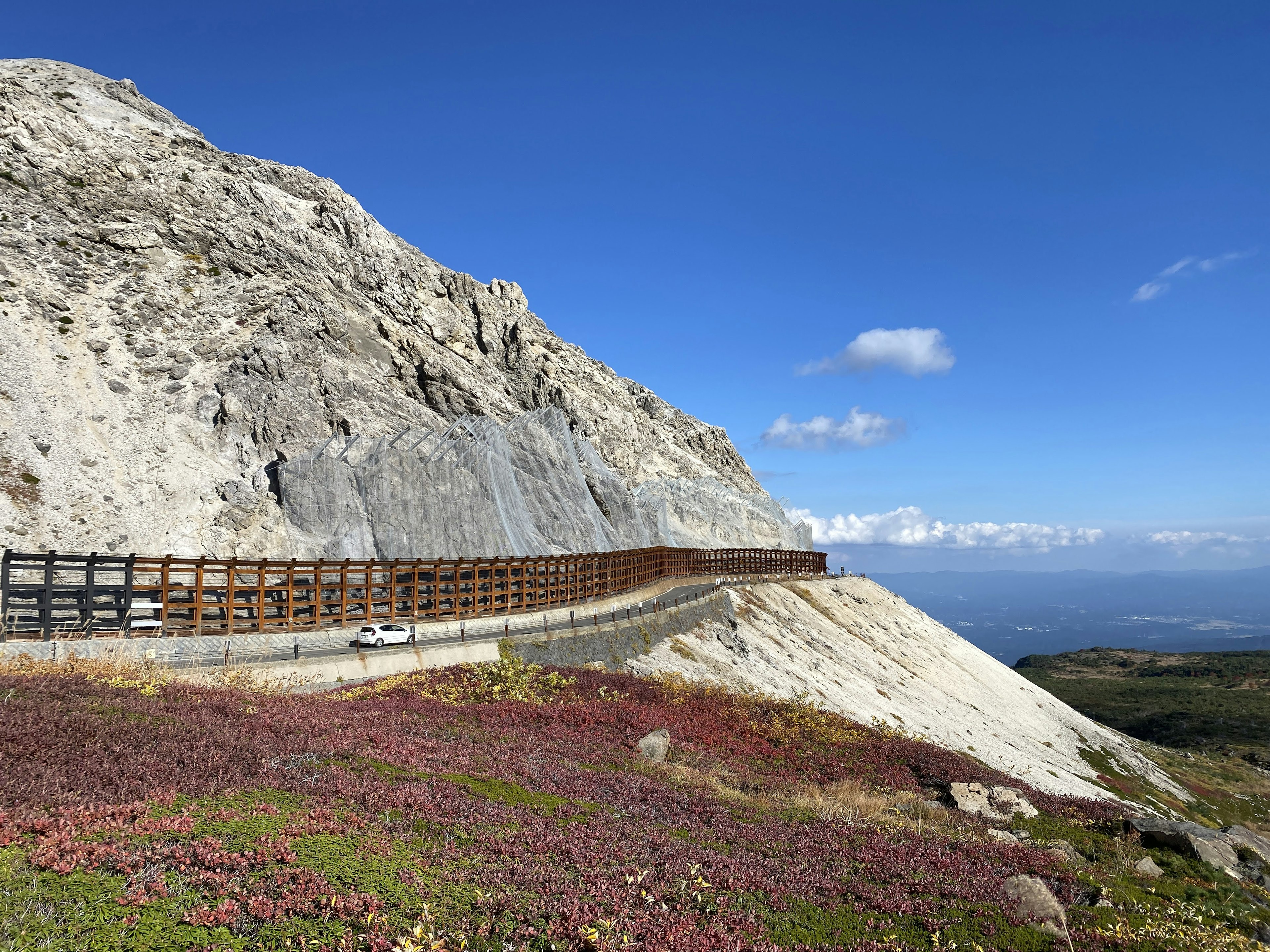 Route sinueuse le long d'une pente rocheuse sous un ciel bleu clair