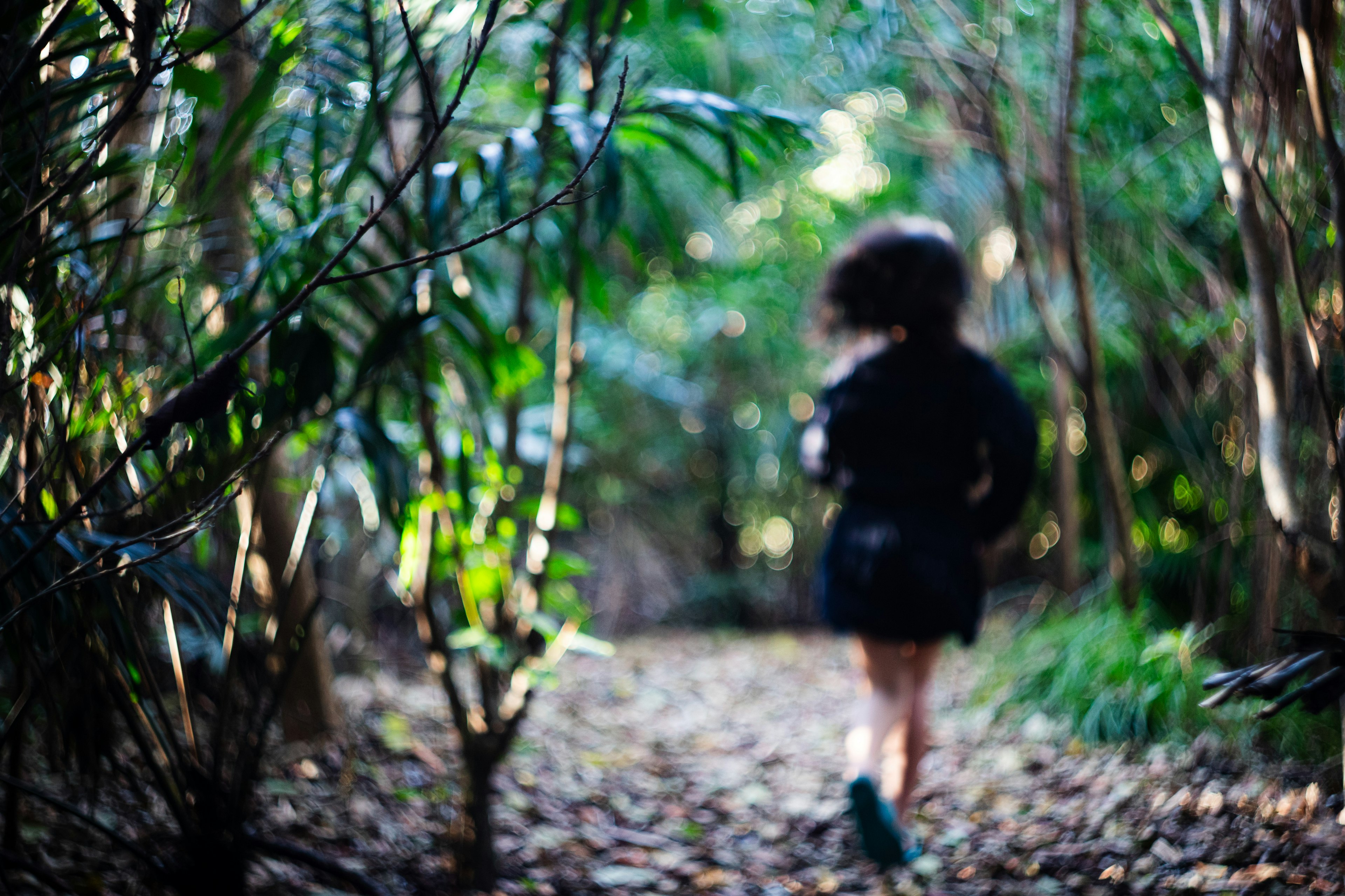 Una donna che corre su un sentiero nel bosco circondata da vegetazione e foglie cadute