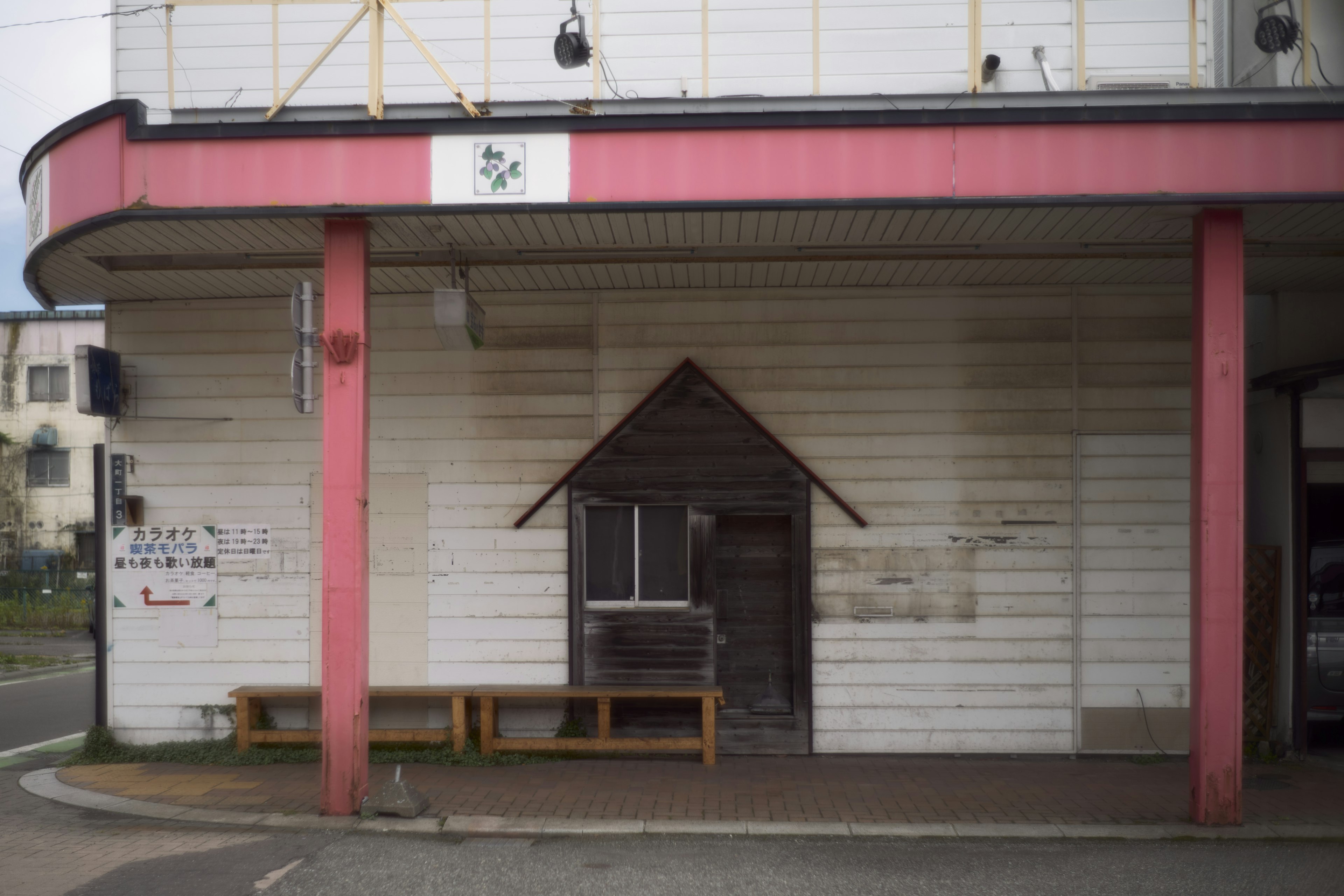 Extérieur d'un bâtiment avec des murs blancs et des piliers roses présentant une petite cabane en bois et des bancs