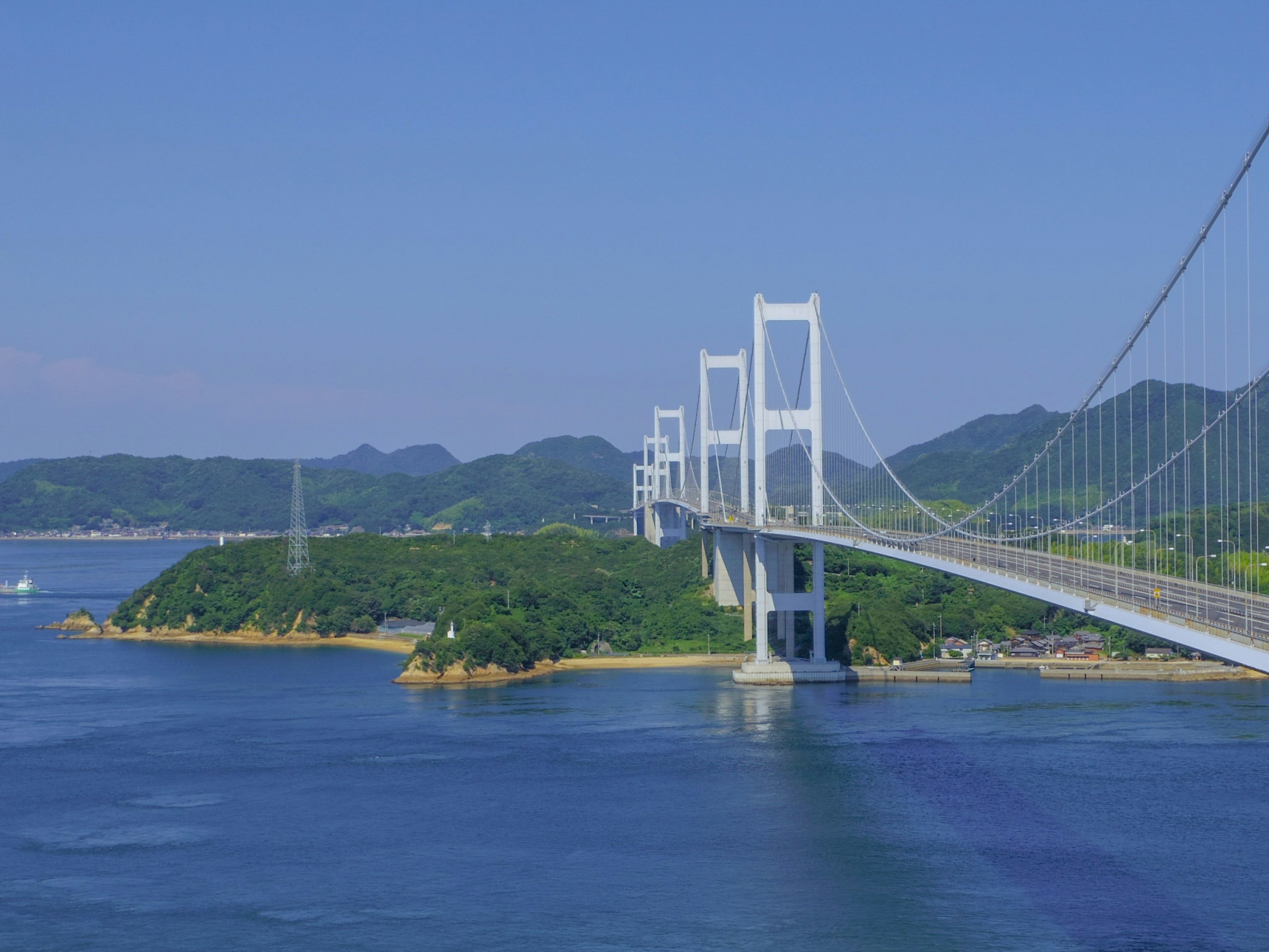 Scenic view of a beautiful white bridge over blue water and green hills