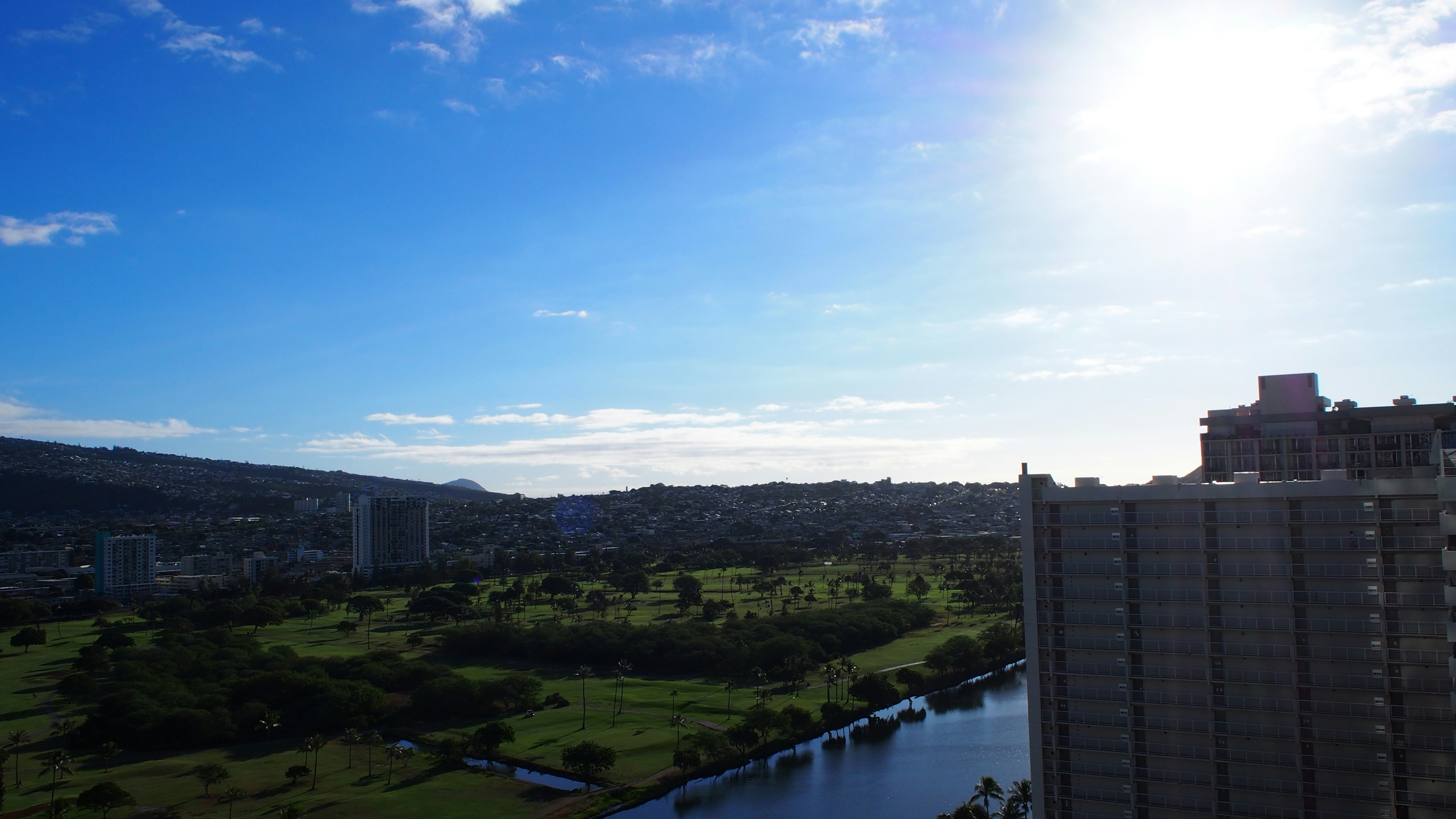 青空と太陽が輝く風景の写真 緑地と川が見える