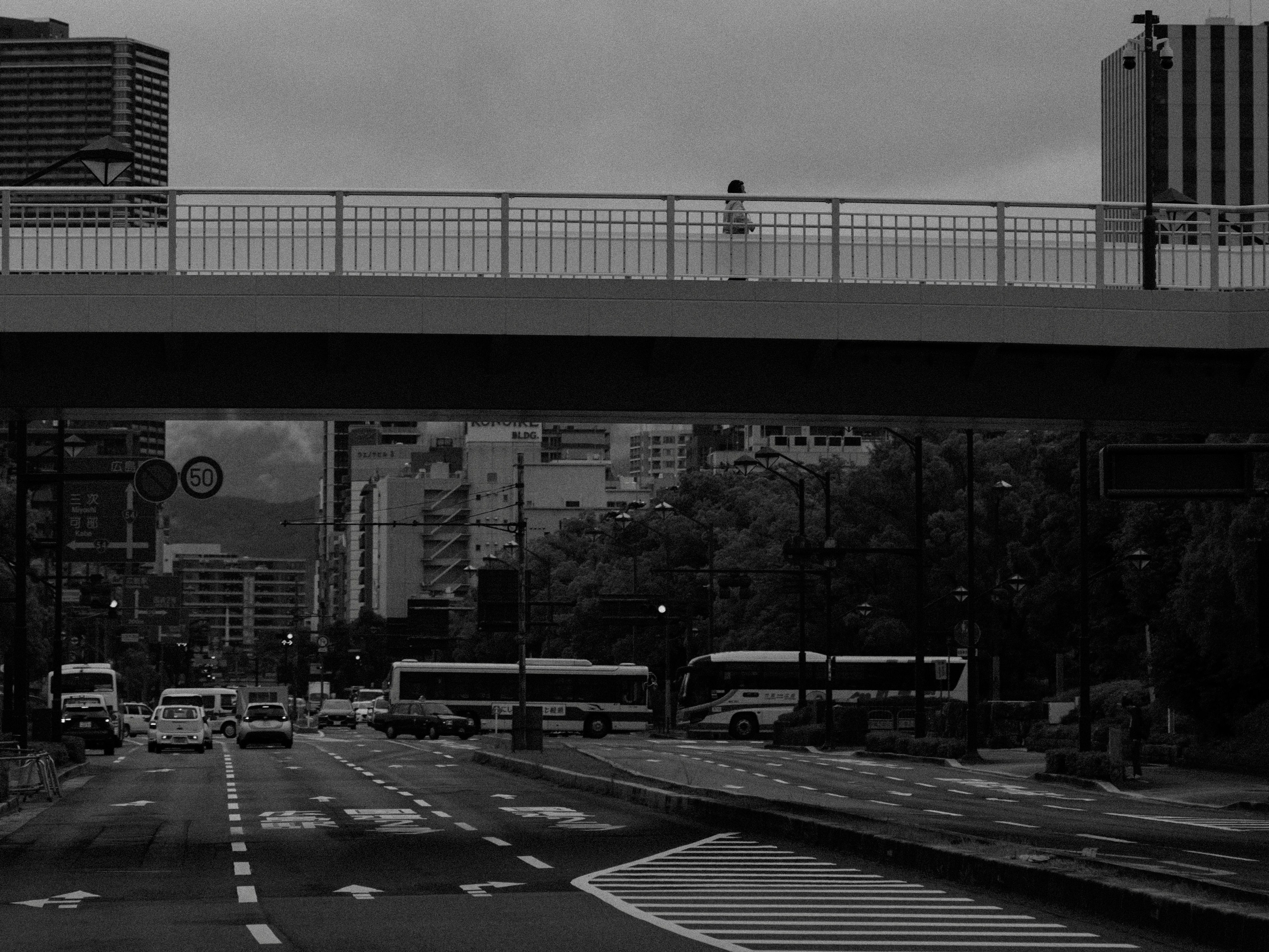 Scena urbana con strada e sovrappasso in bianco e nero con una persona sul ponte