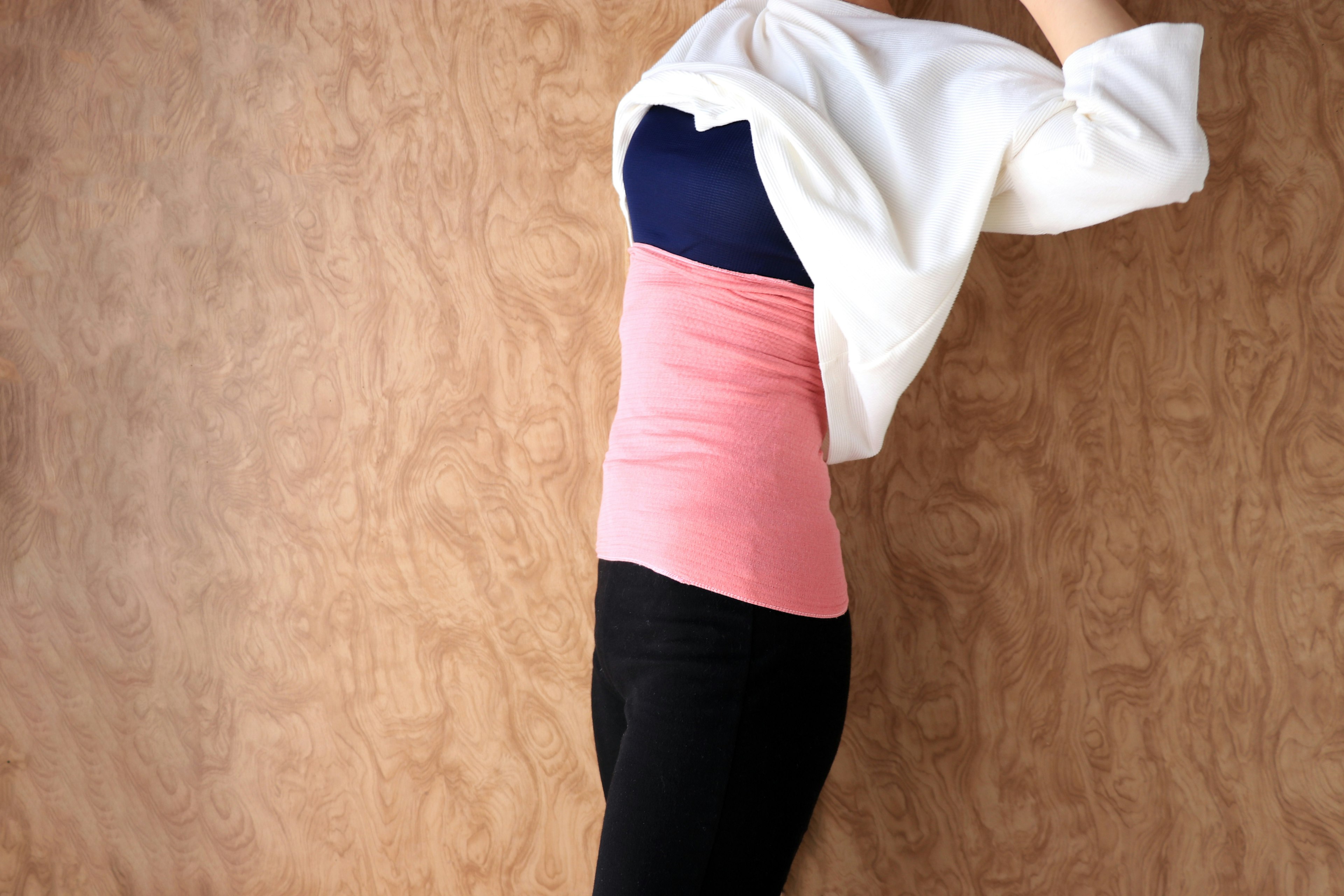 Woman wearing a white cardigan with a pink top and black leggings posing against a wooden background