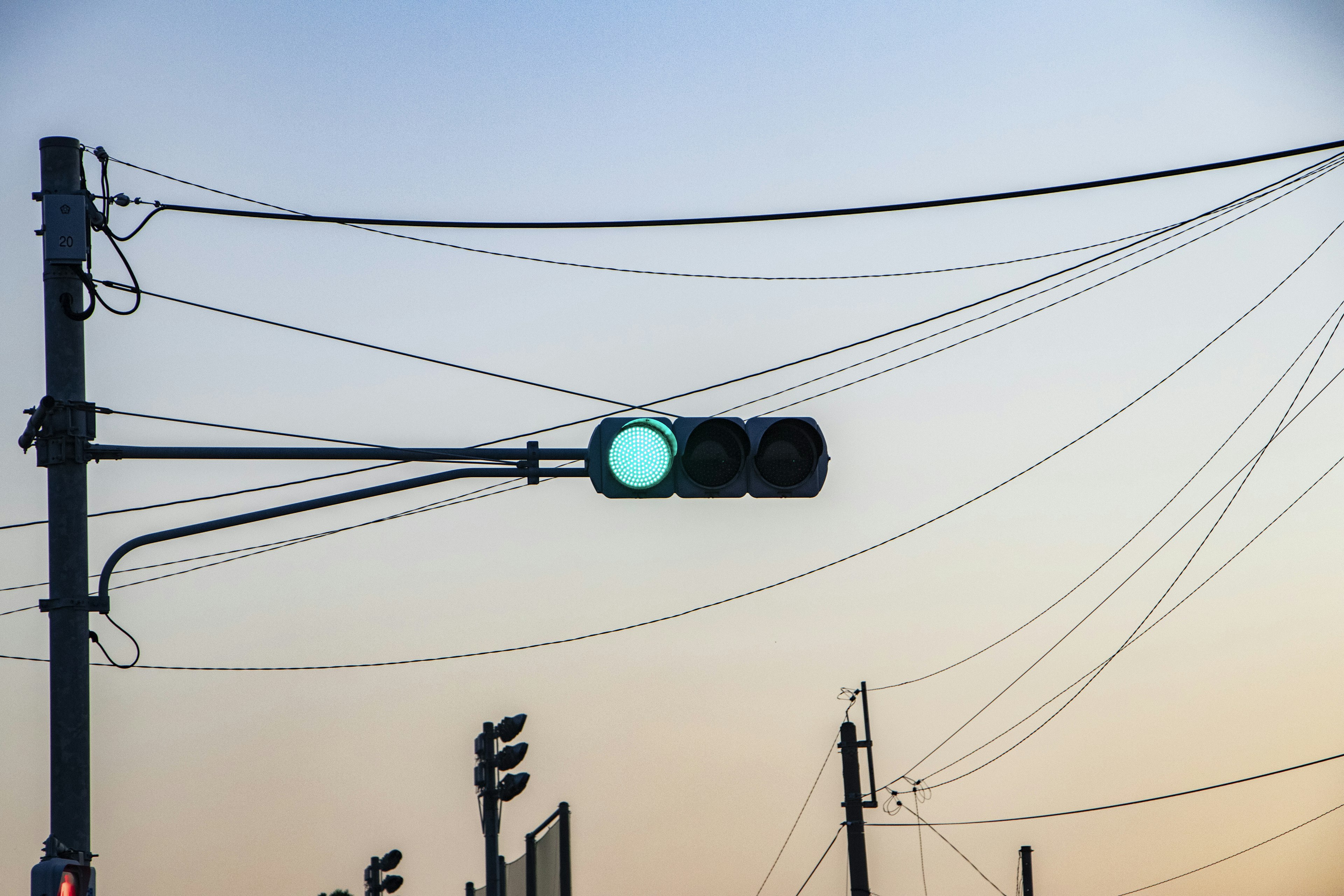 Lampu lalu lintas hijau dan kabel listrik di latar belakang langit senja