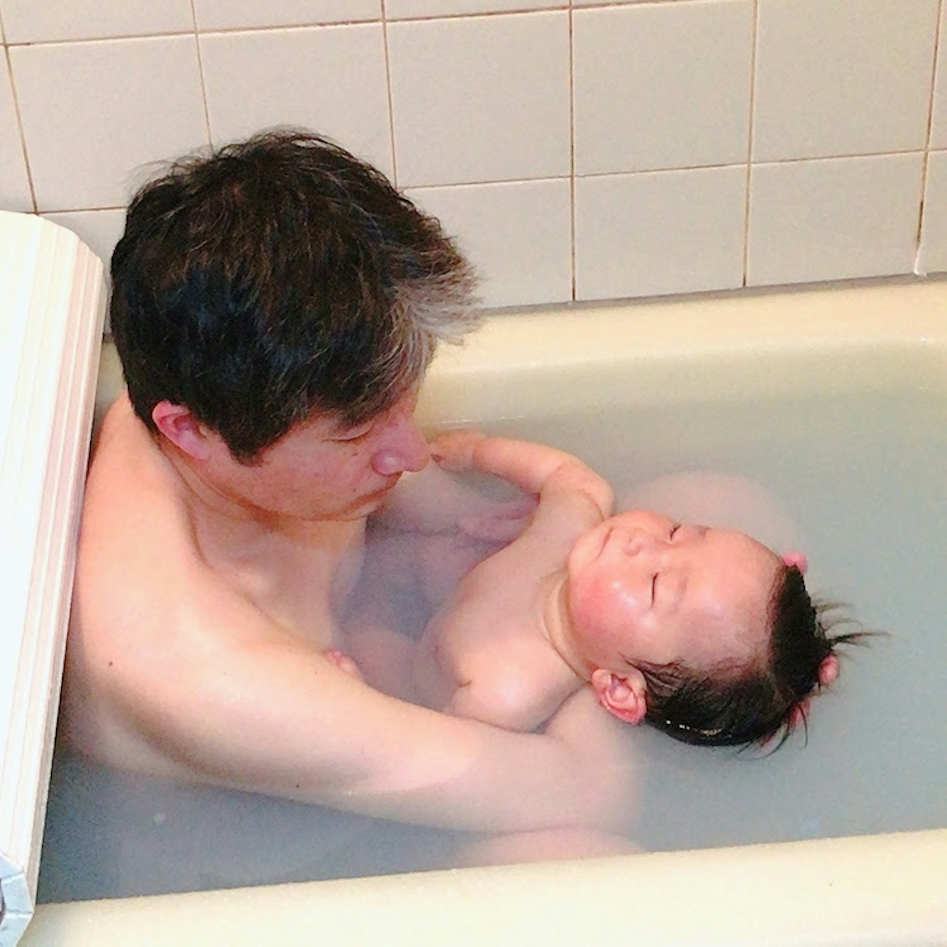 Ein Vater hält ein Baby in einer Badewanne