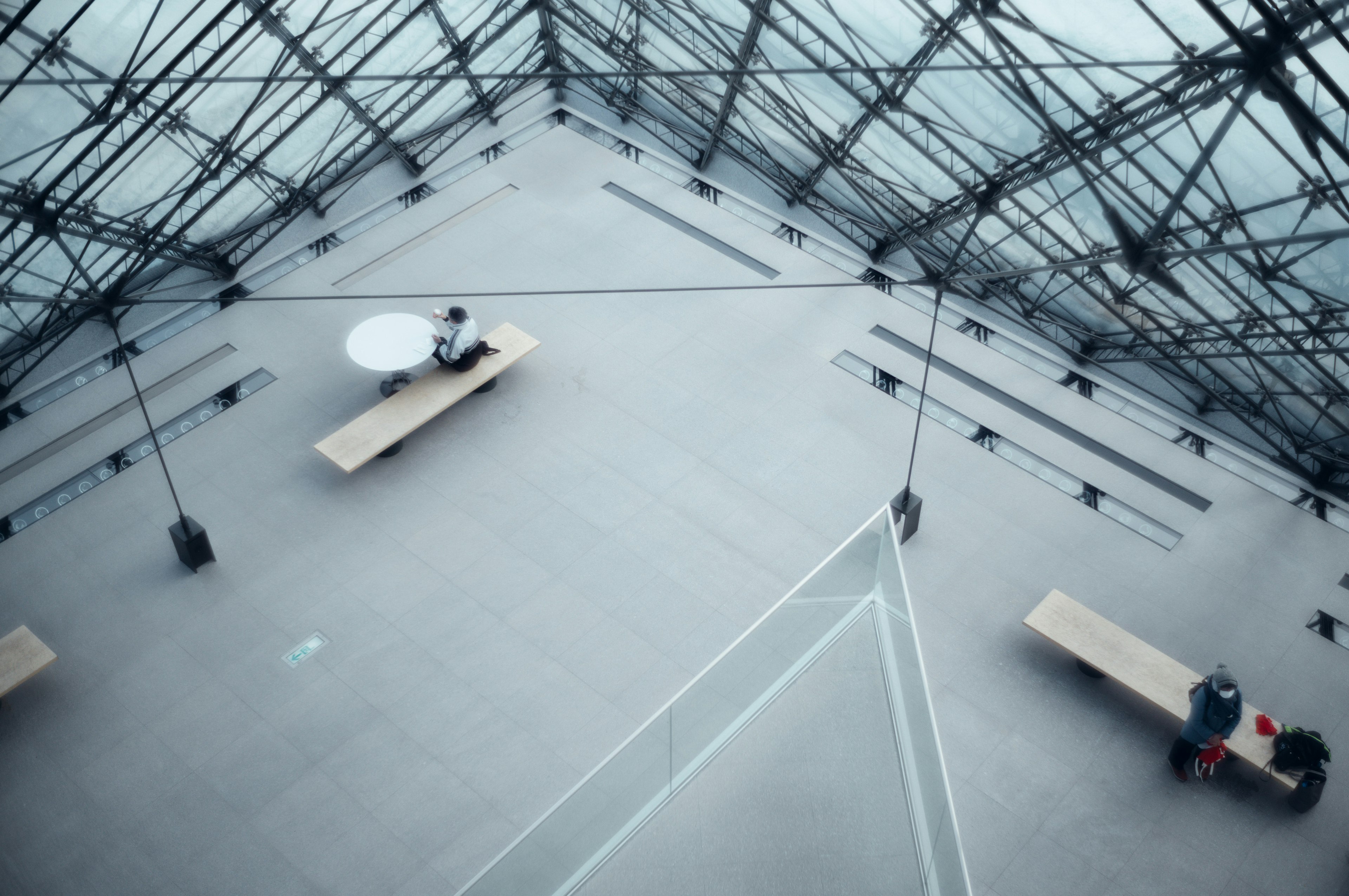 Interior view of the Louvre Museum under the glass pyramid featuring benches