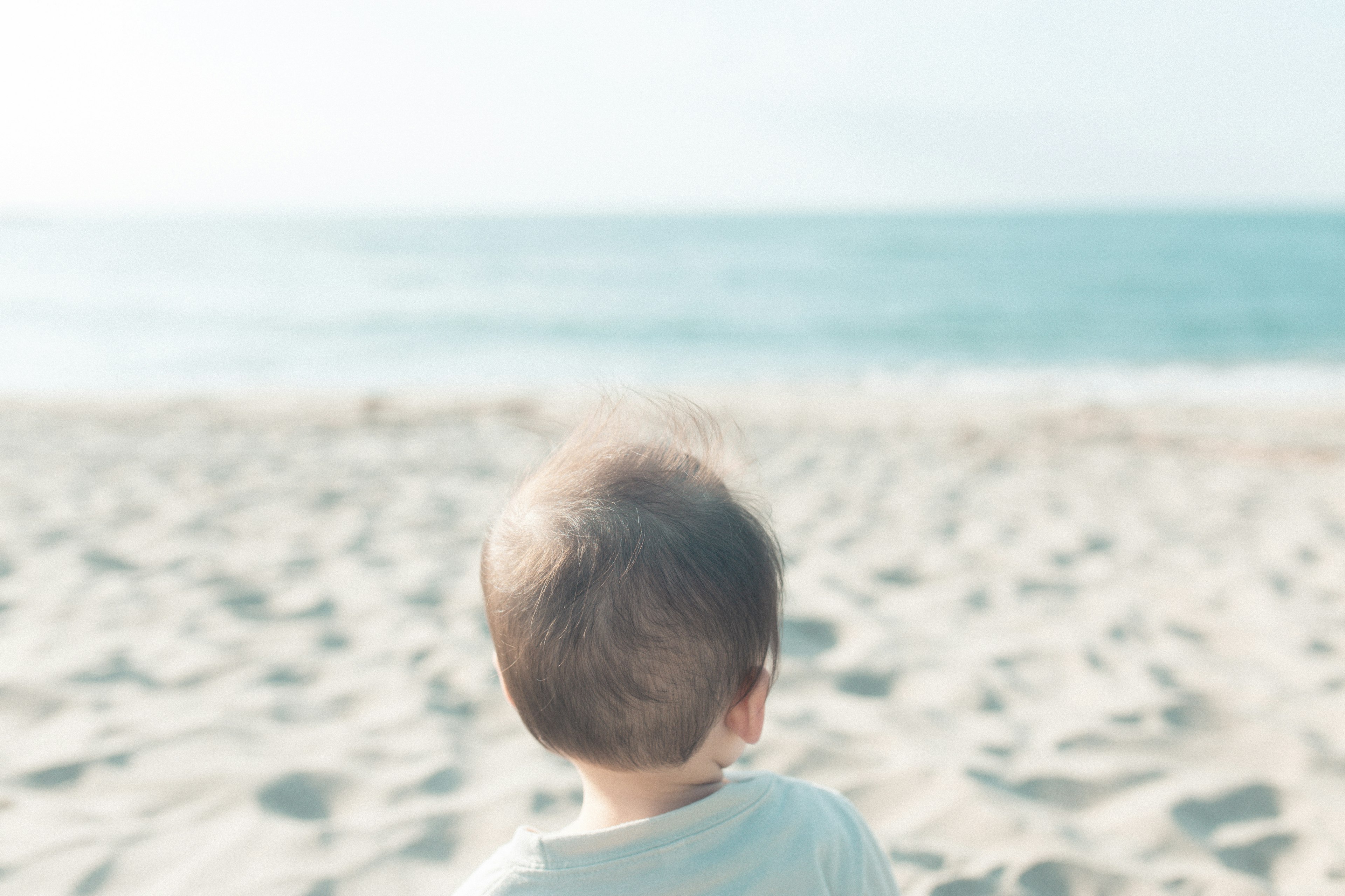 A baby sitting on the sandy beach gazing at the ocean