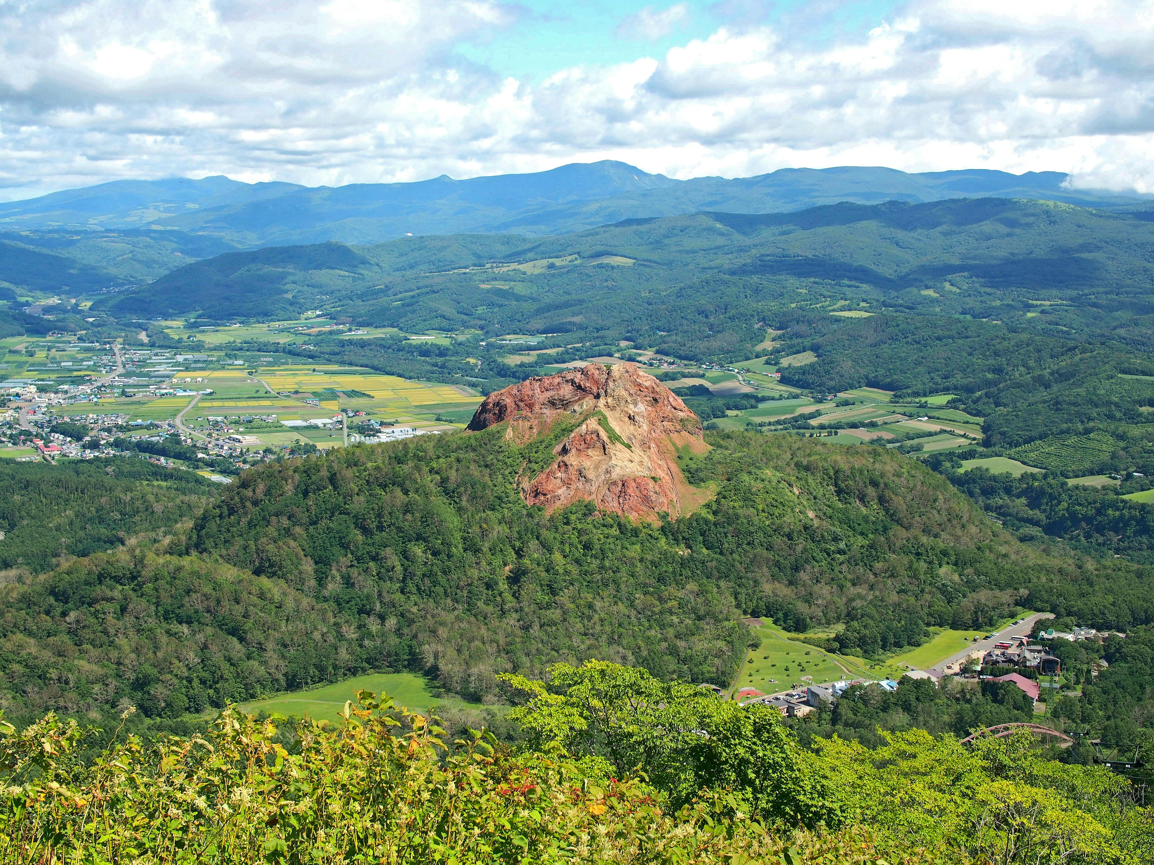 Pemandangan gunung merah dikelilingi perbukitan hijau