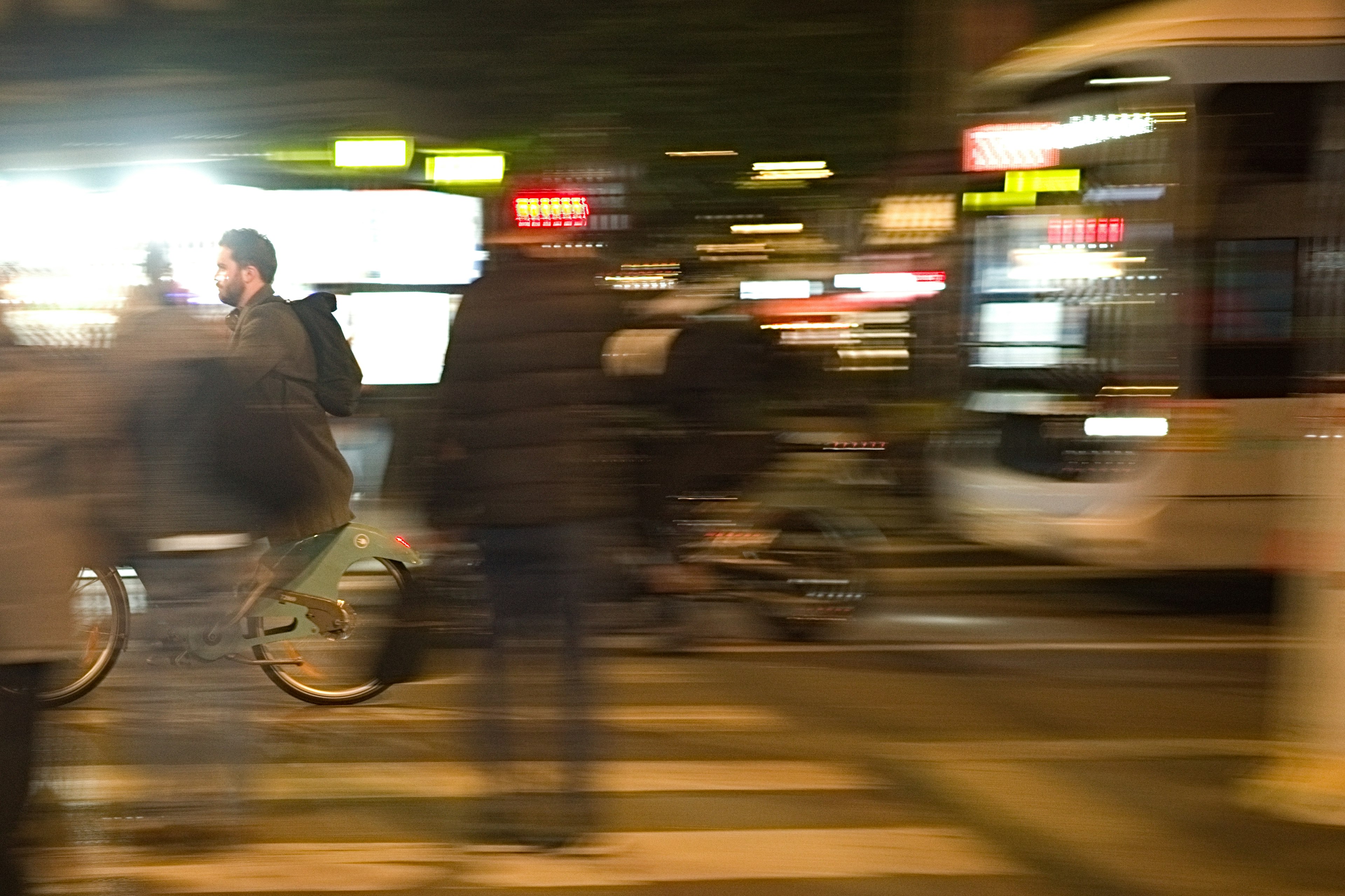 Adegan kabur seorang pengendara sepeda dan pejalan kaki yang menyeberang persimpangan di malam hari