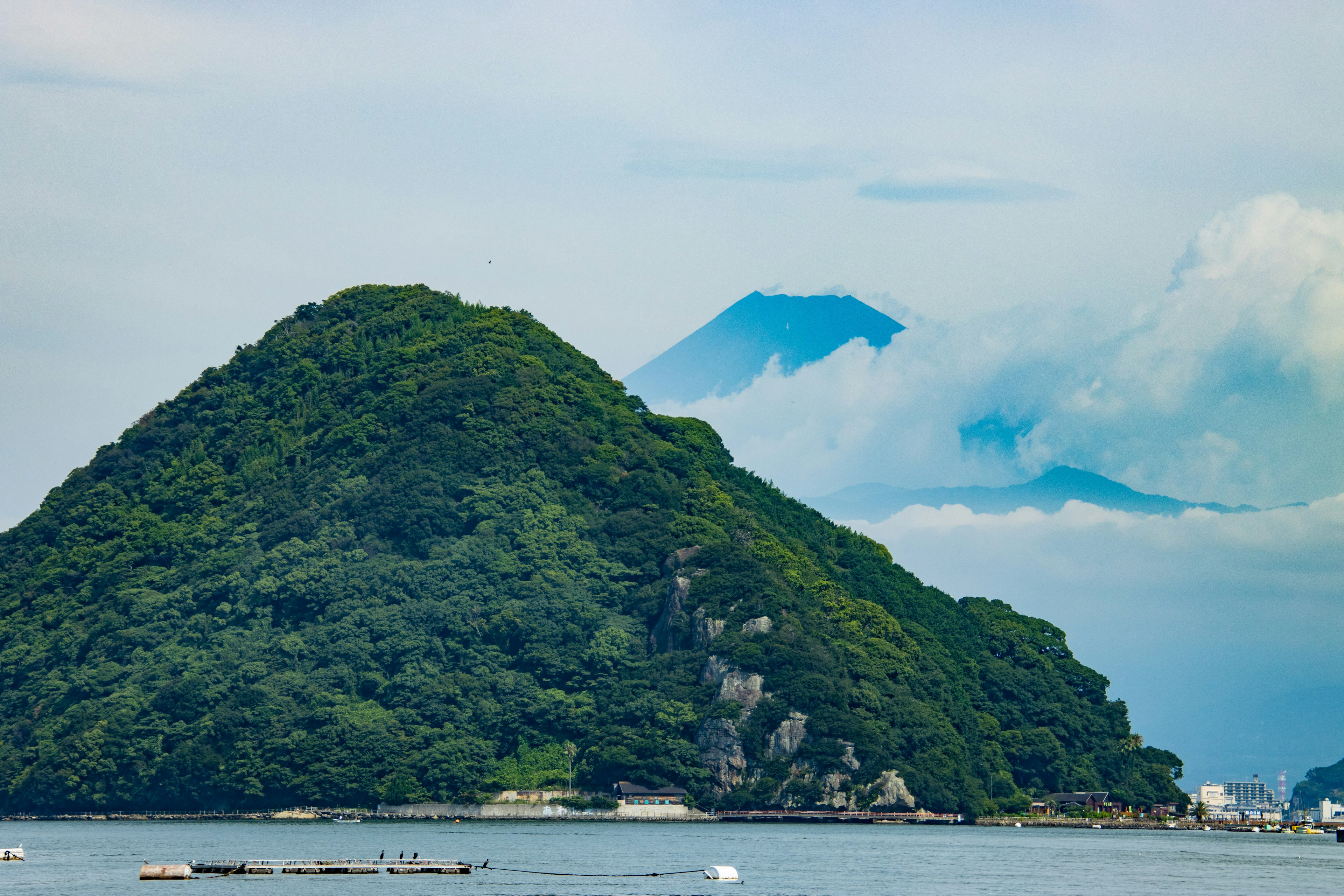 Green mountain under blue sky with distant view of Mount Fuji