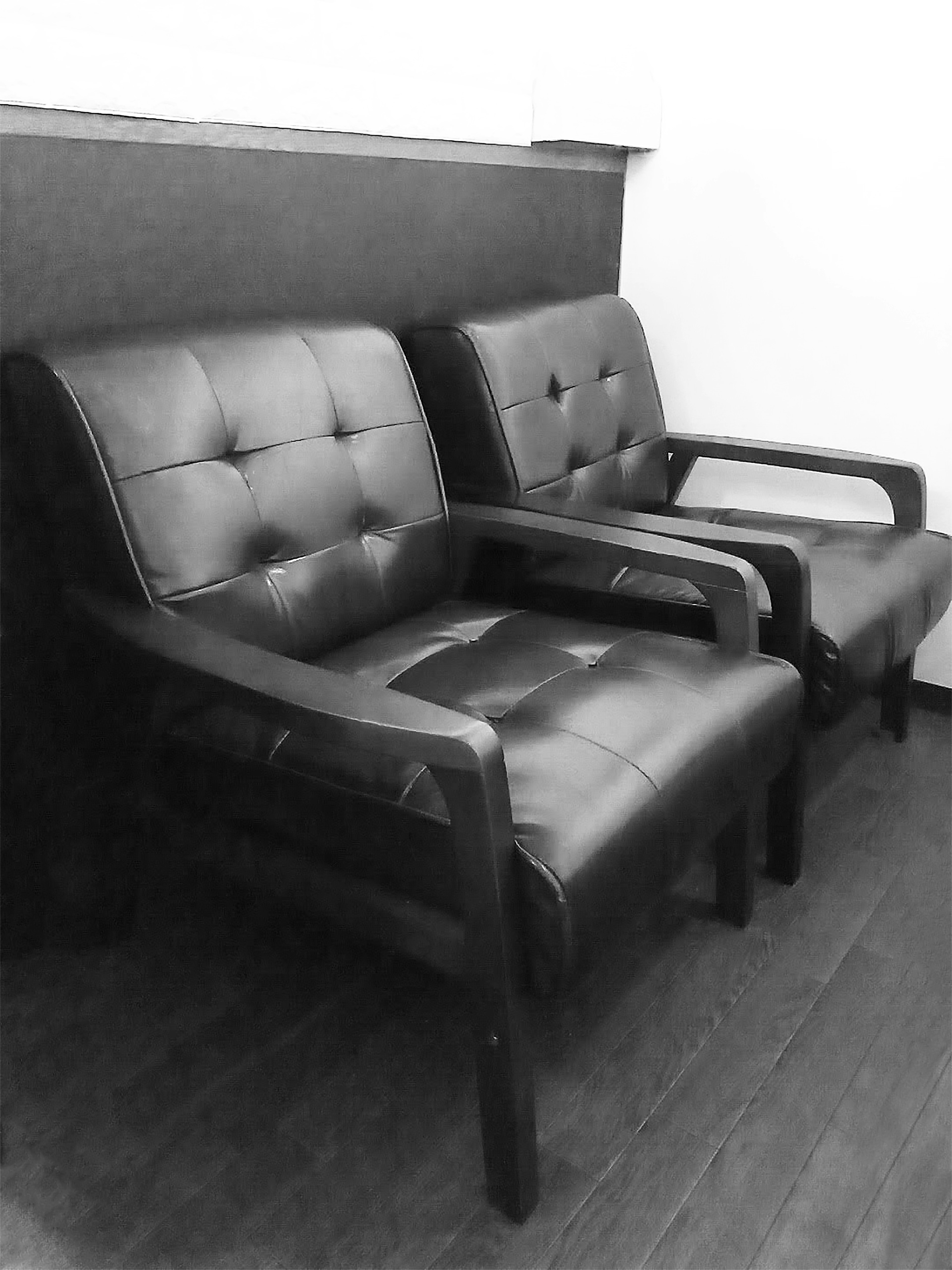 Two black leather chairs positioned side by side in a simple indoor setting