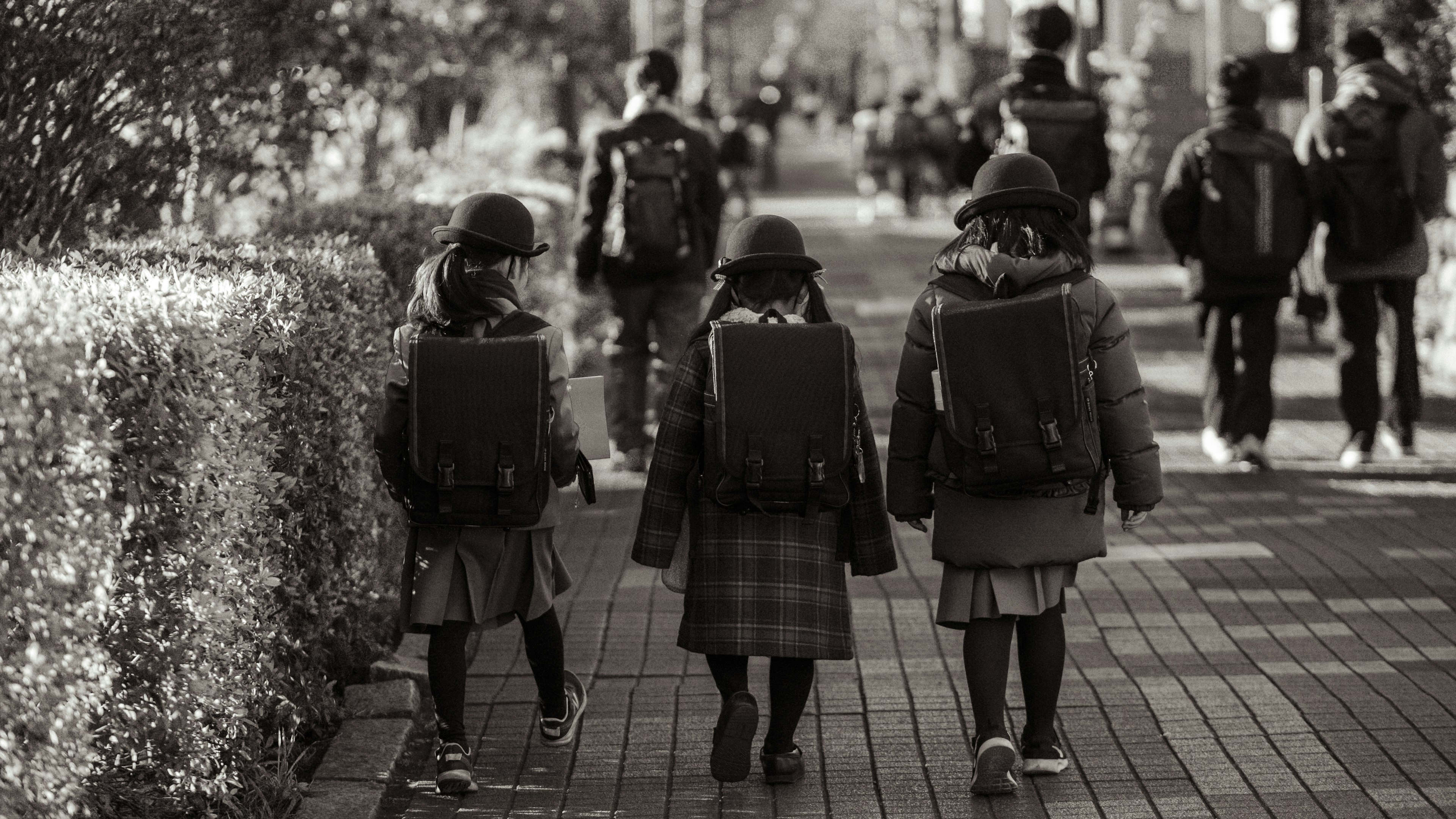 Dos niños caminando con mochilas en una escena urbana en blanco y negro