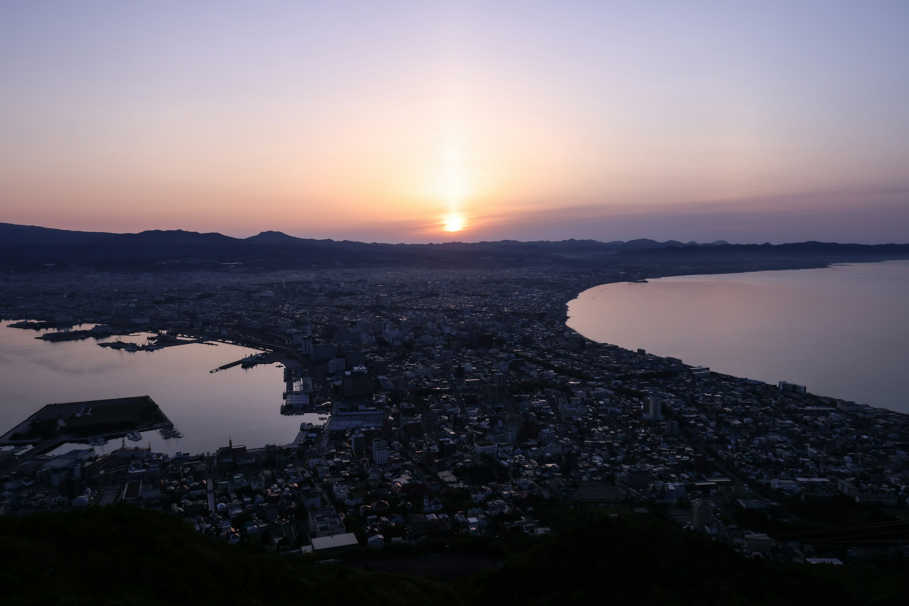 Panoramic view of a city at sunset surrounded by sea and mountains