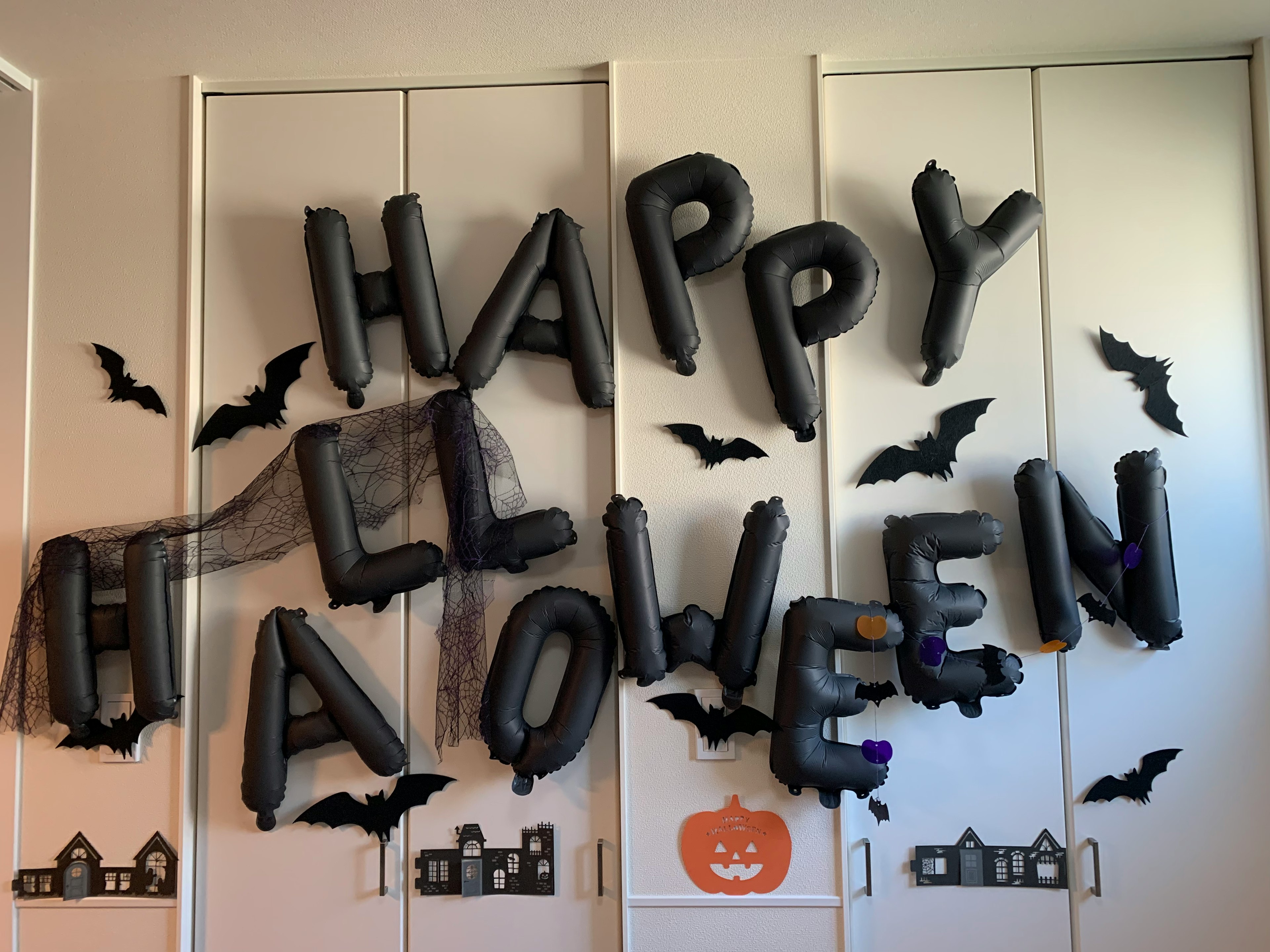 Decorazione di Halloween con palloncini neri che scrivono 'HAPPY HALLOWEEN' insieme a pipistrelli e ragnatele