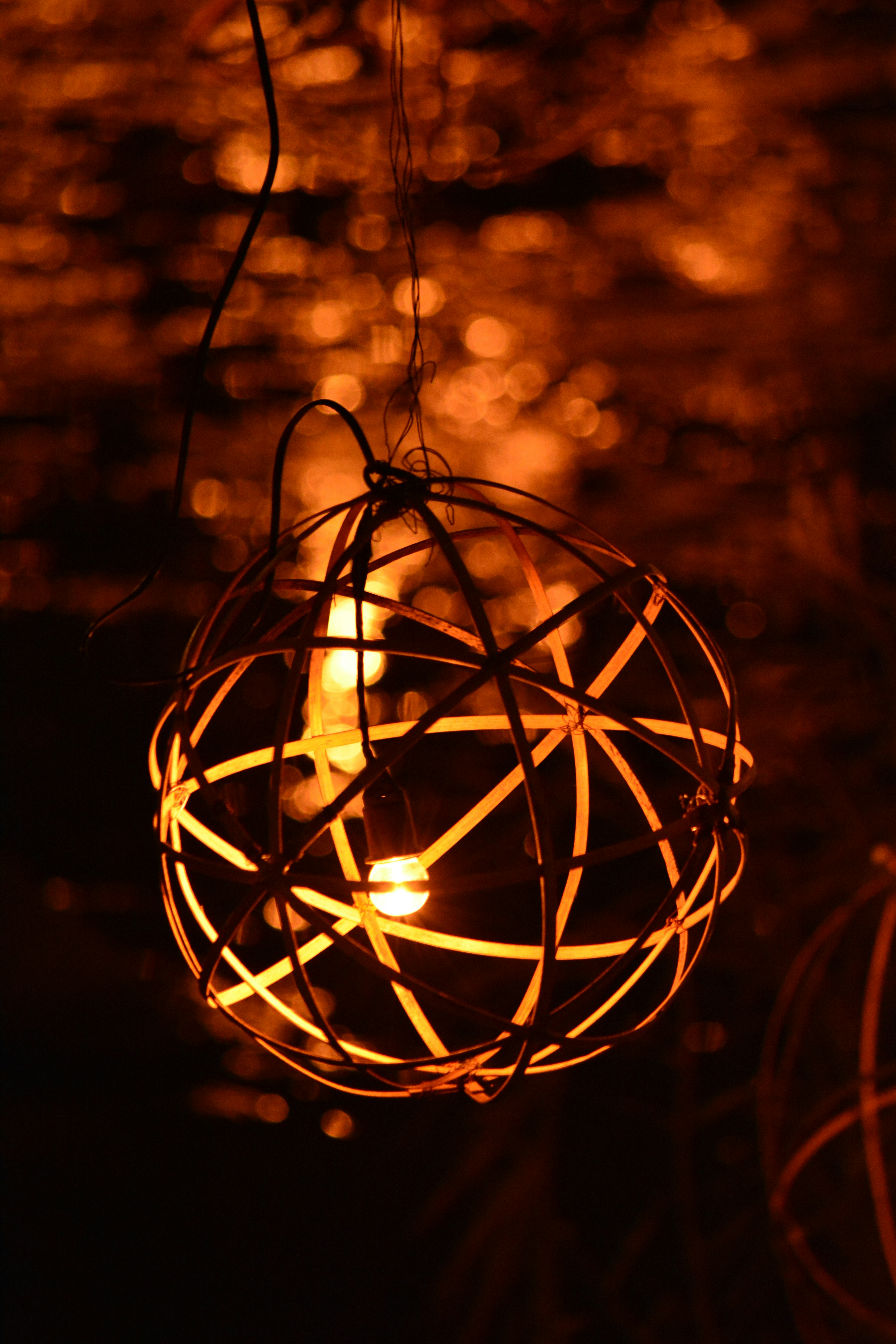 Lámpara esférica decorativa que emite luz naranja cálida colgando en un fondo oscuro