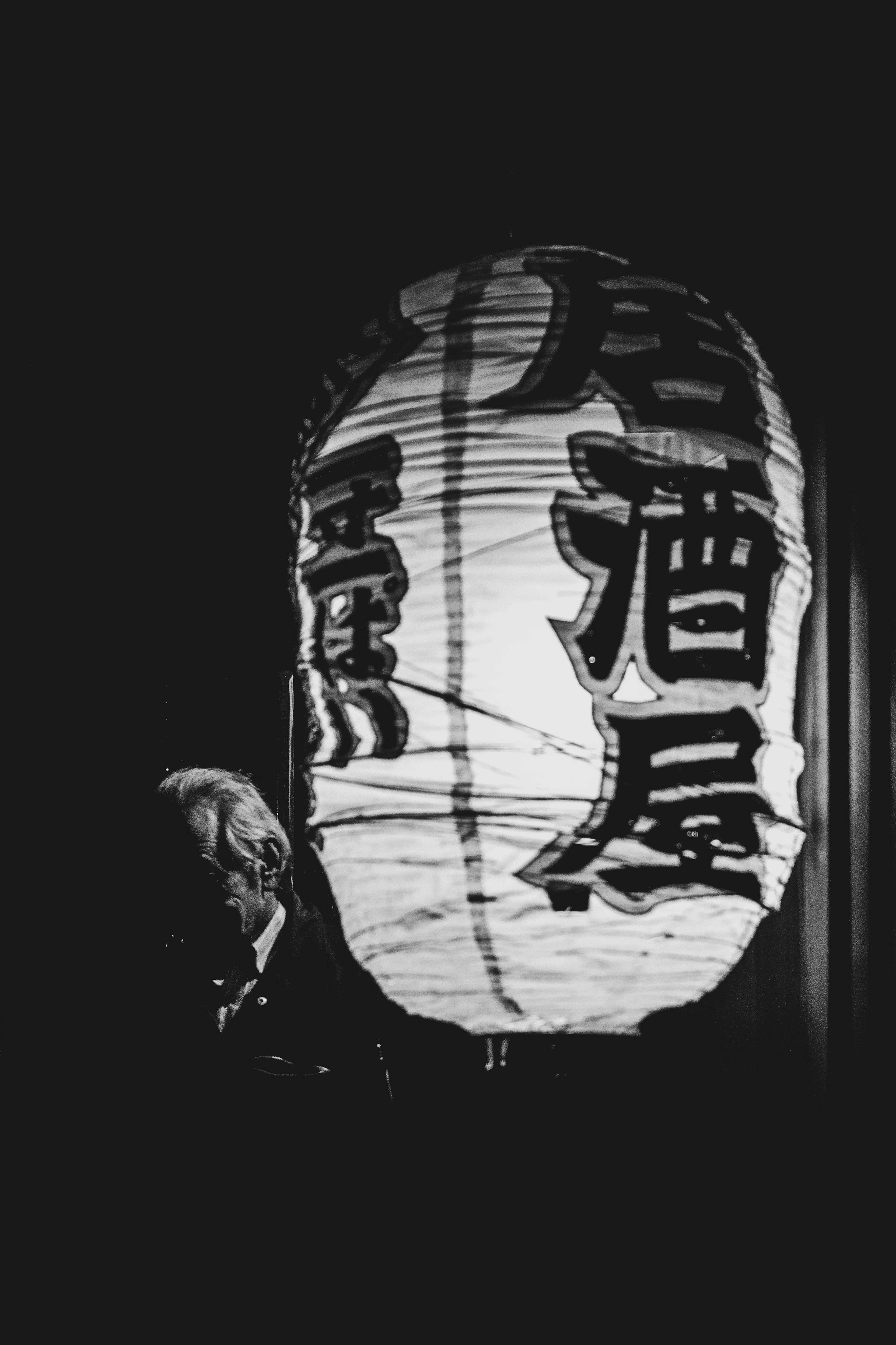 A white lantern illuminated against a dark background featuring kanji characters