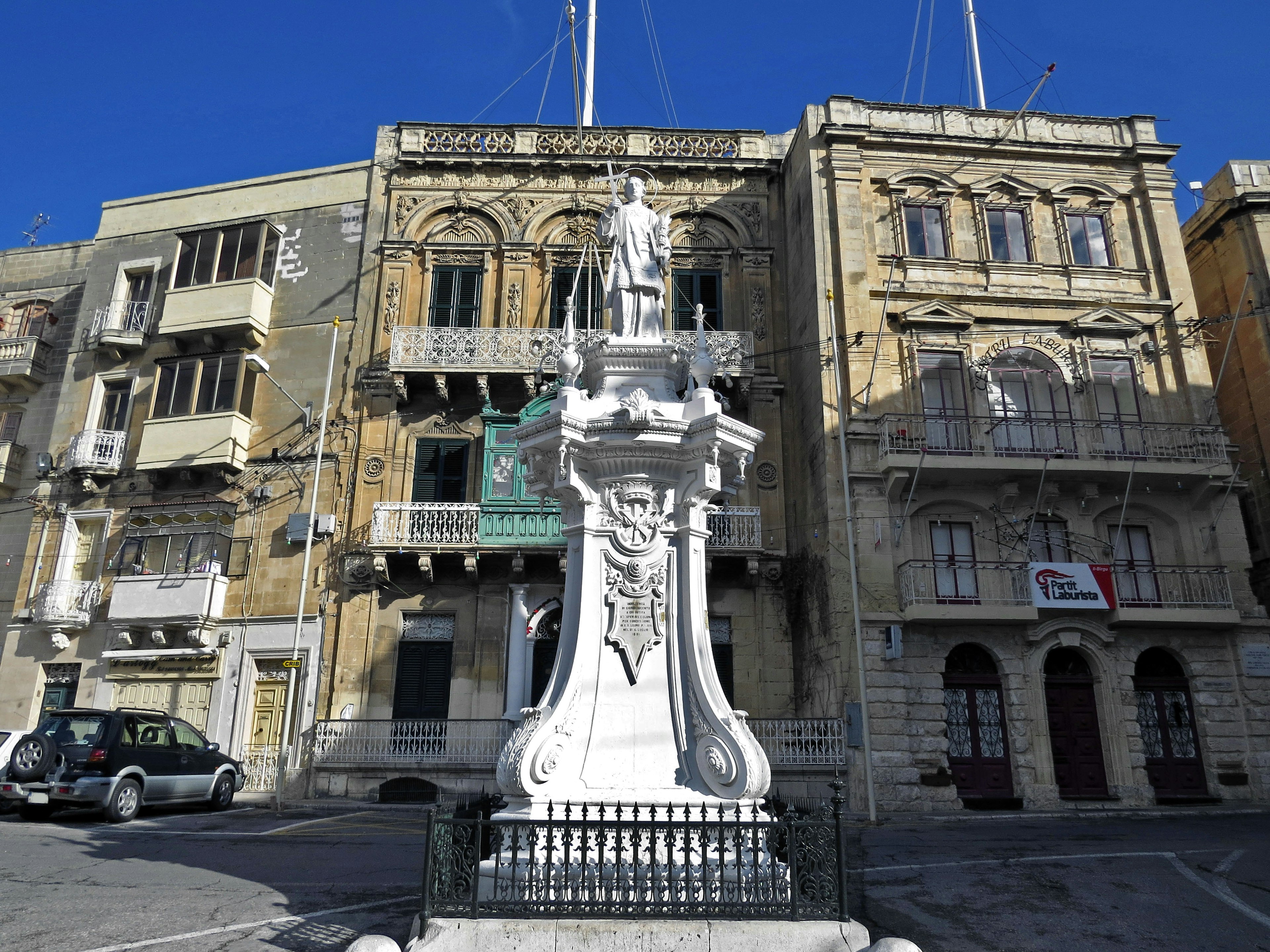 Ein Platz mit einer weißen Statue umgeben von historischen Gebäuden und einem klaren blauen Himmel