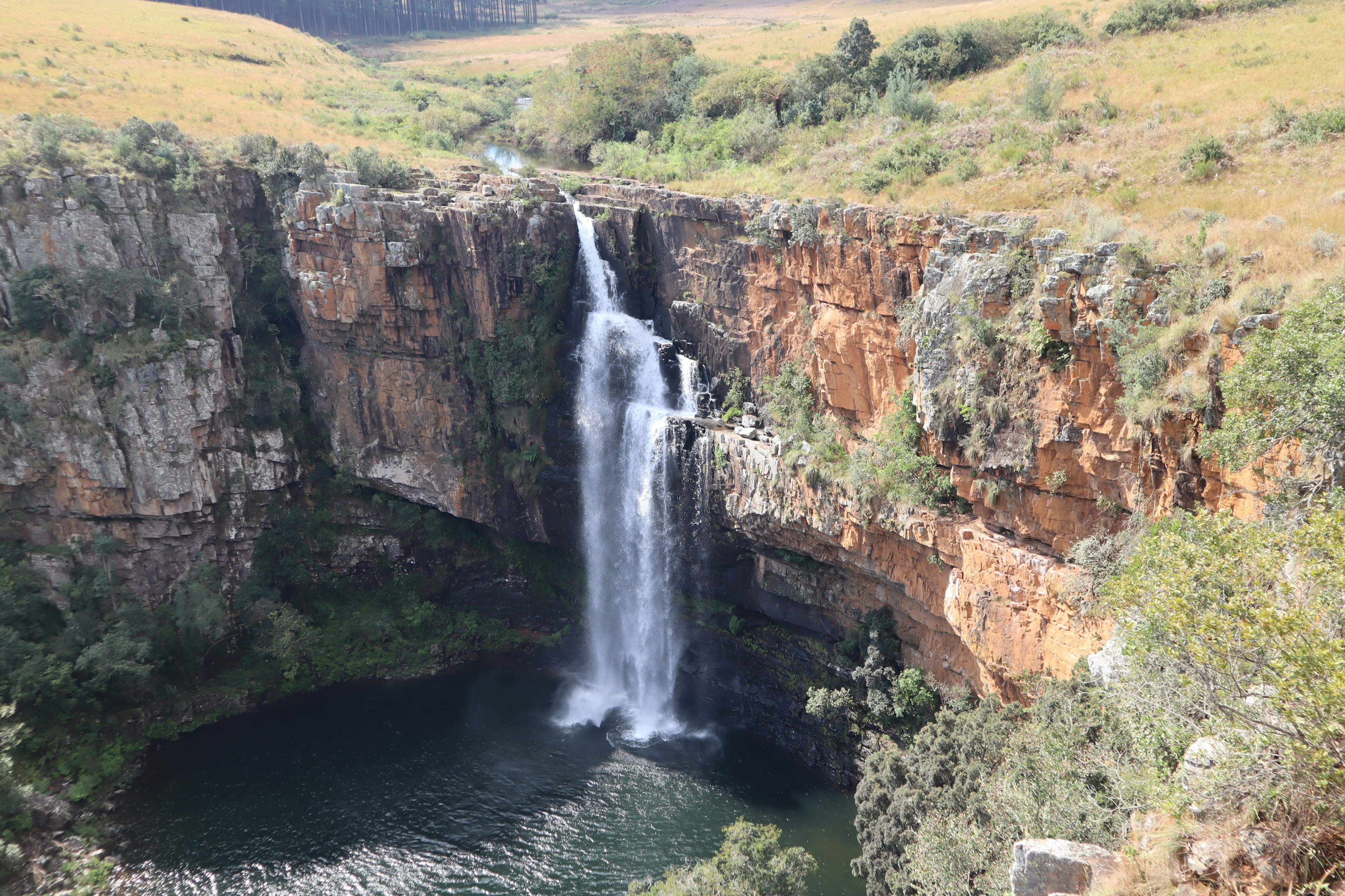 Eine atemberaubende Landschaft mit einem Wasserfall, der von felsigen Klippen in üppiges Grün stürzt