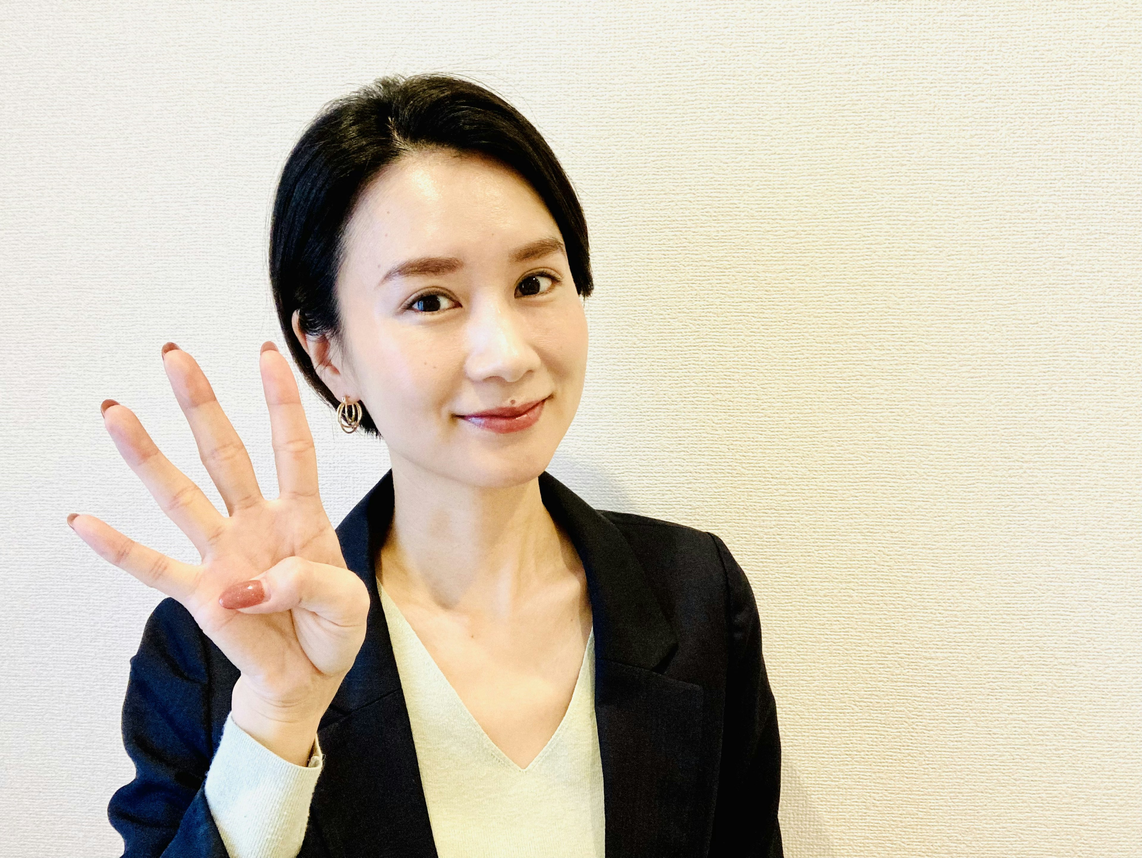 A woman smiling and holding up four fingers in a business attire photo