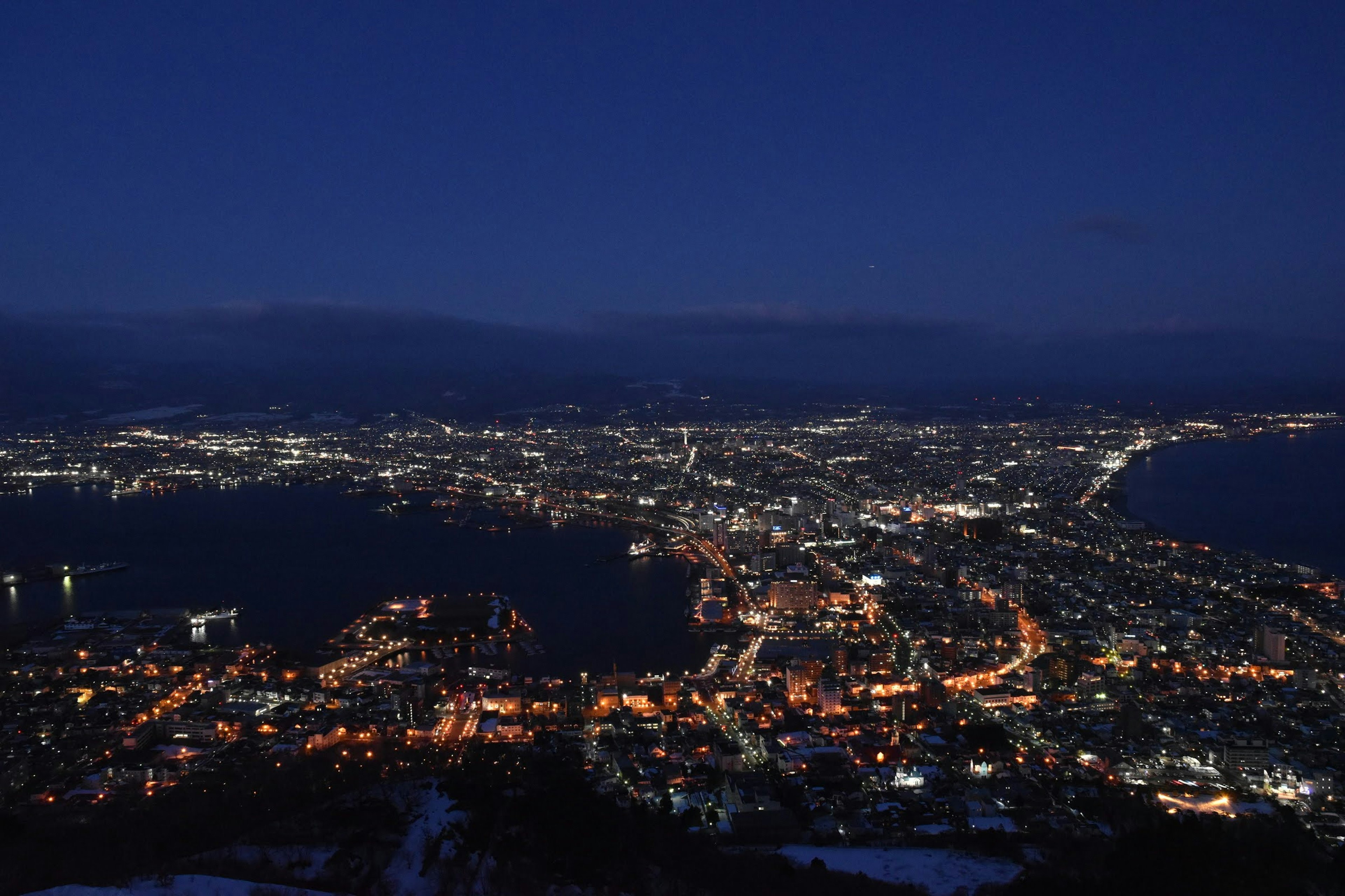 Panoramablick auf die nächtliche Stadt Hakodate mit Lichtern und Ozean