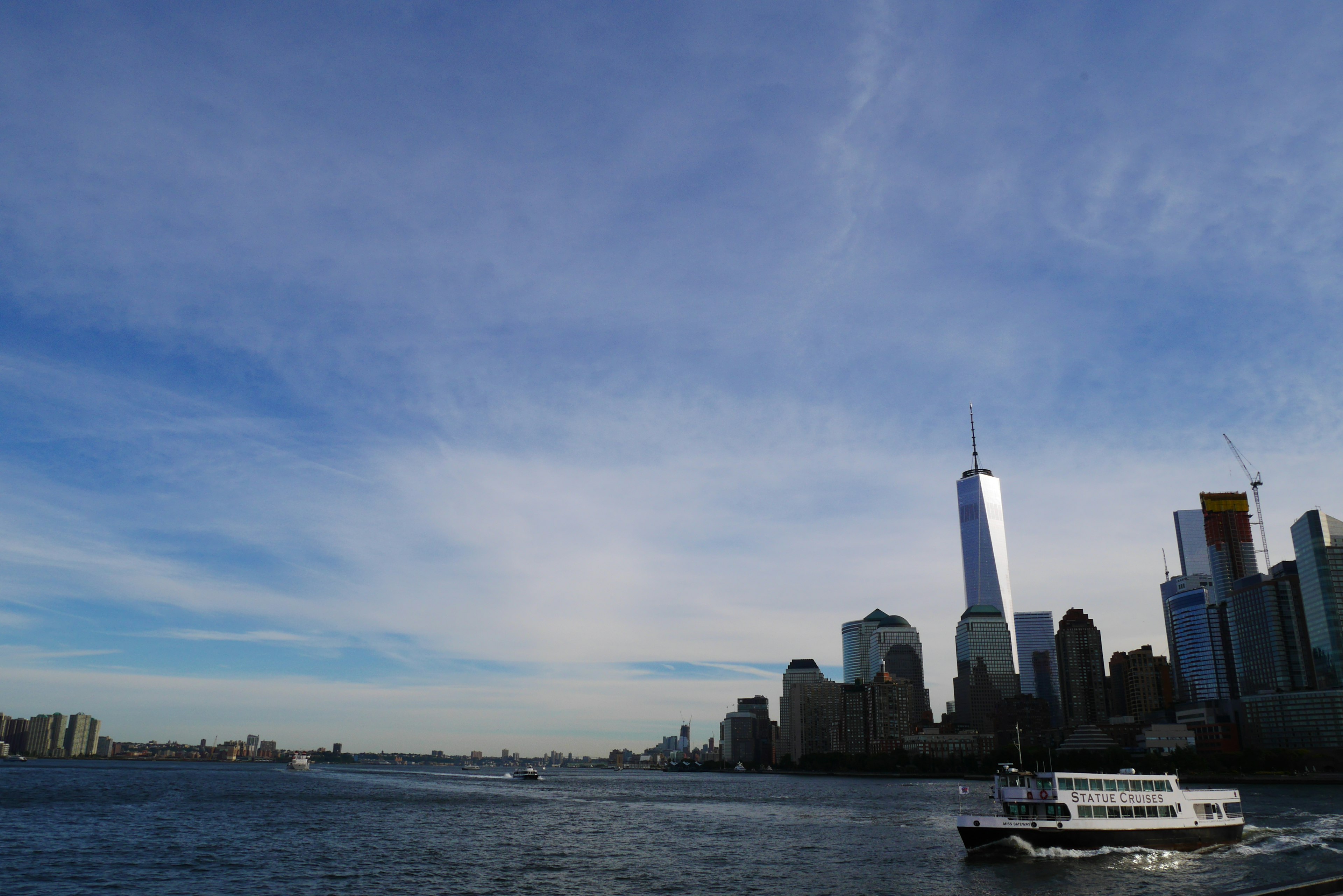 New York skyline featuring One World Trade Center against a blue sky and water view