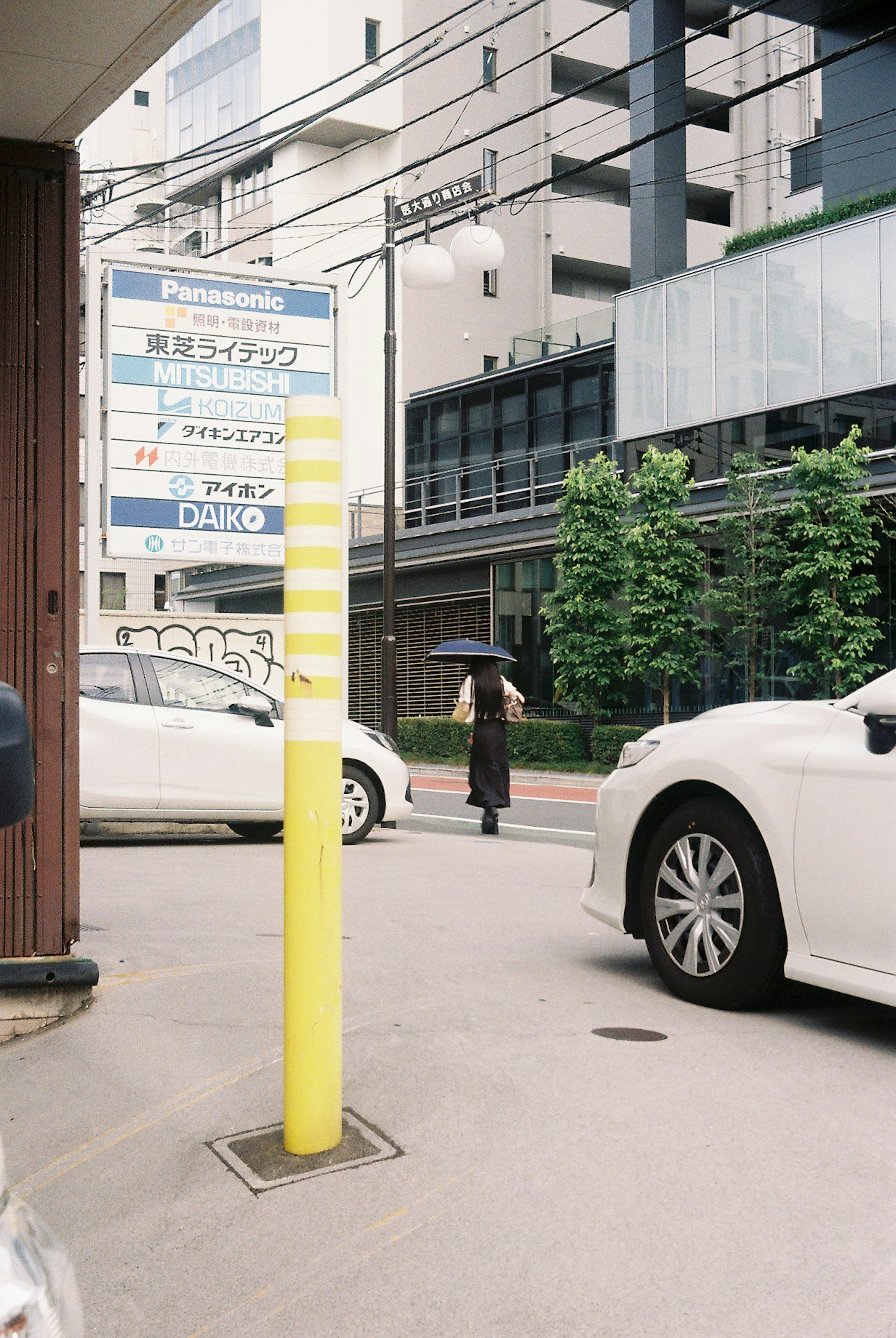 Une vue urbaine avec un poteau jaune et des voitures blanches, une personne tenant un parapluie marchant