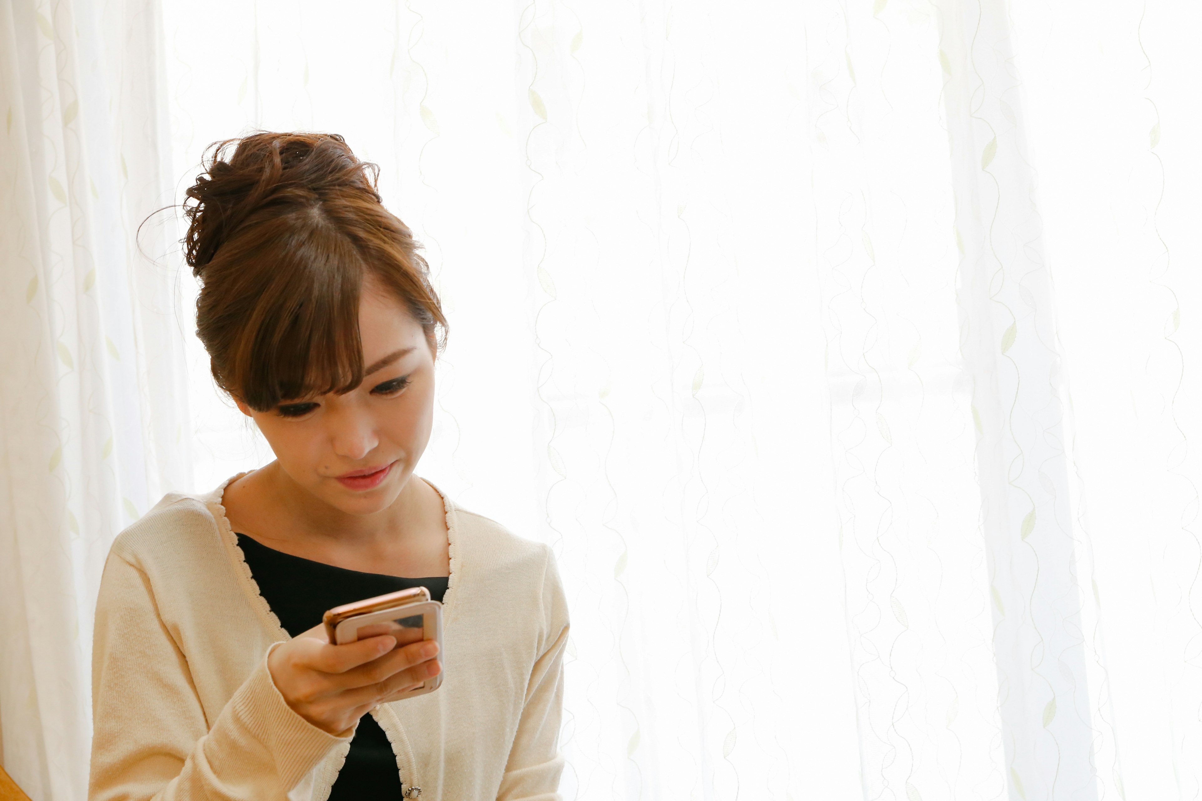 A woman looking at her smartphone with natural light streaming through a window