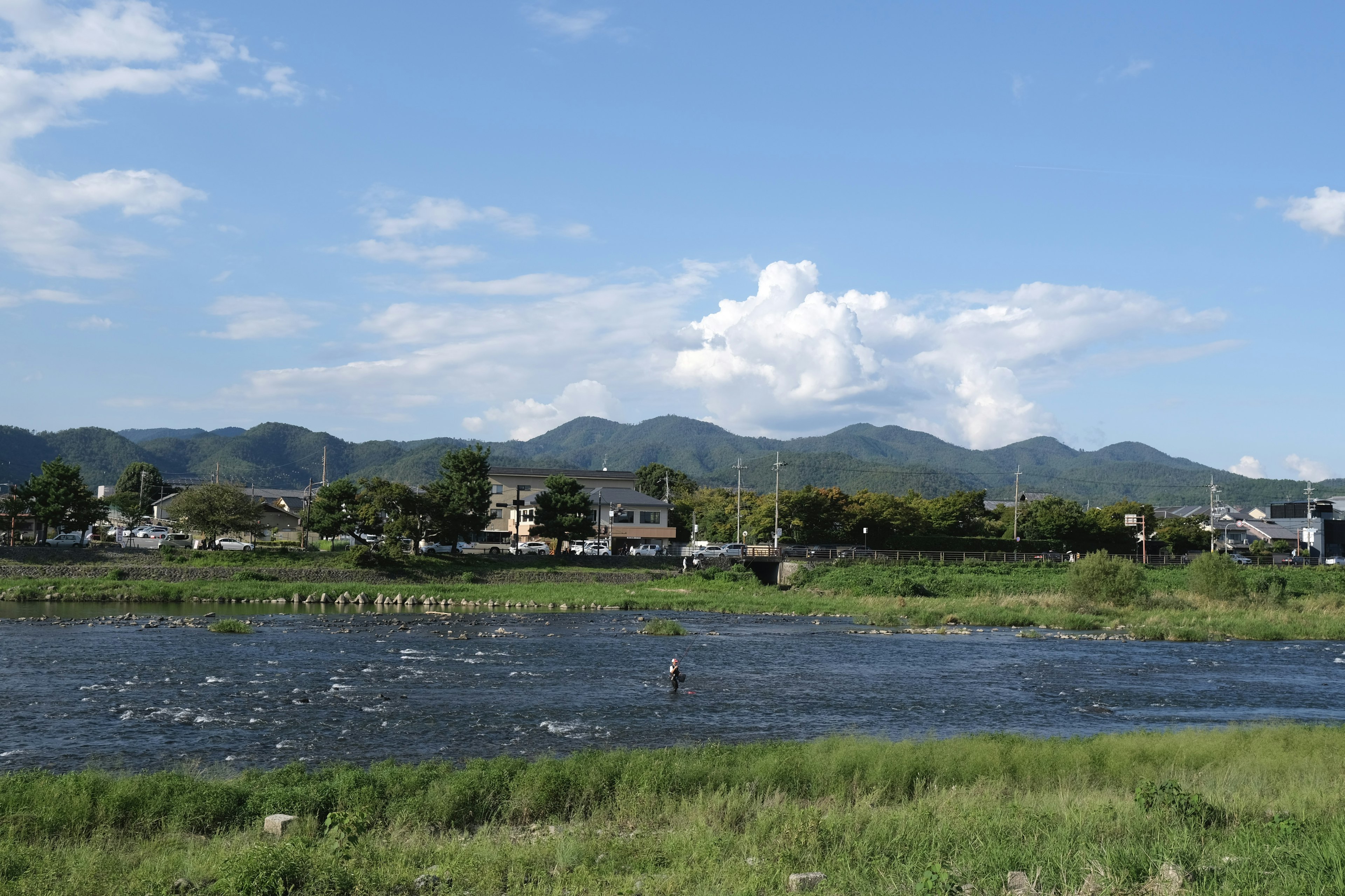 Scenic view of a river under a blue sky with mountains in the background and green grass nearby