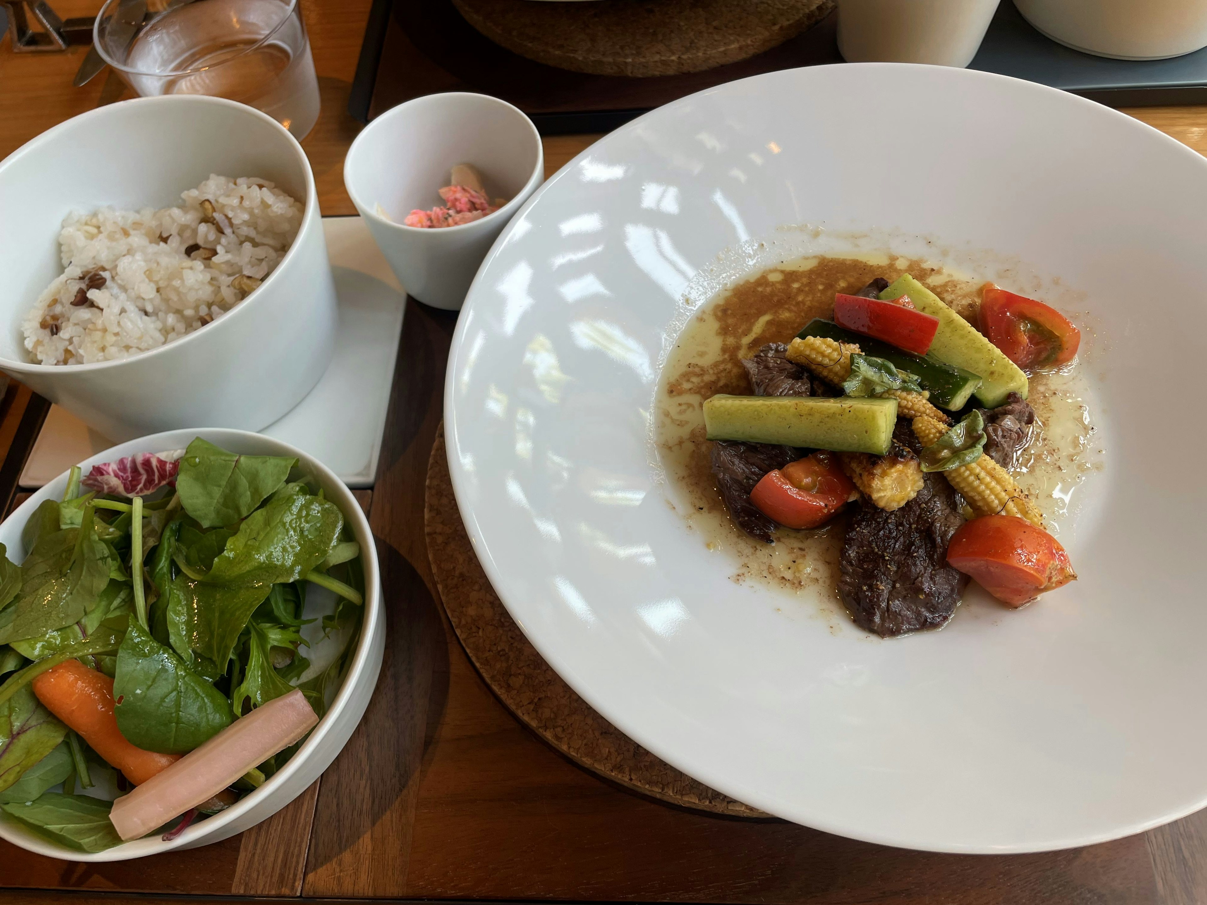 Dish of vegetables and meat served on a white plate with rice and salad