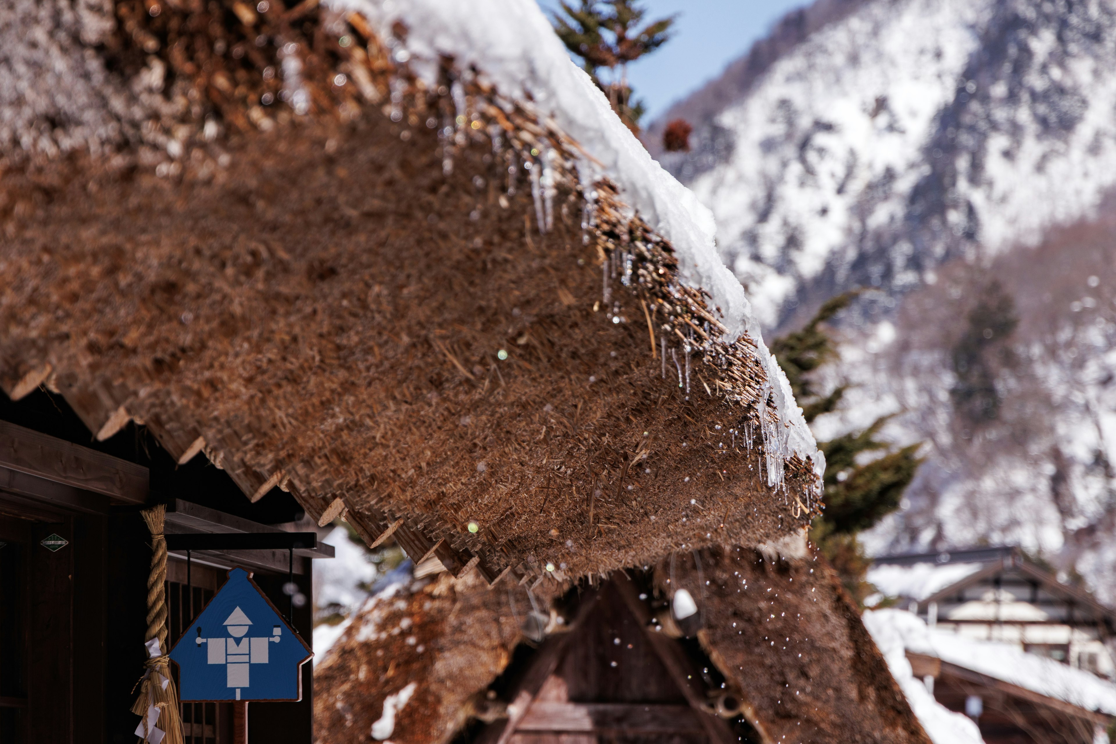 传统茅草屋顶覆盖着雪，背景是山脉