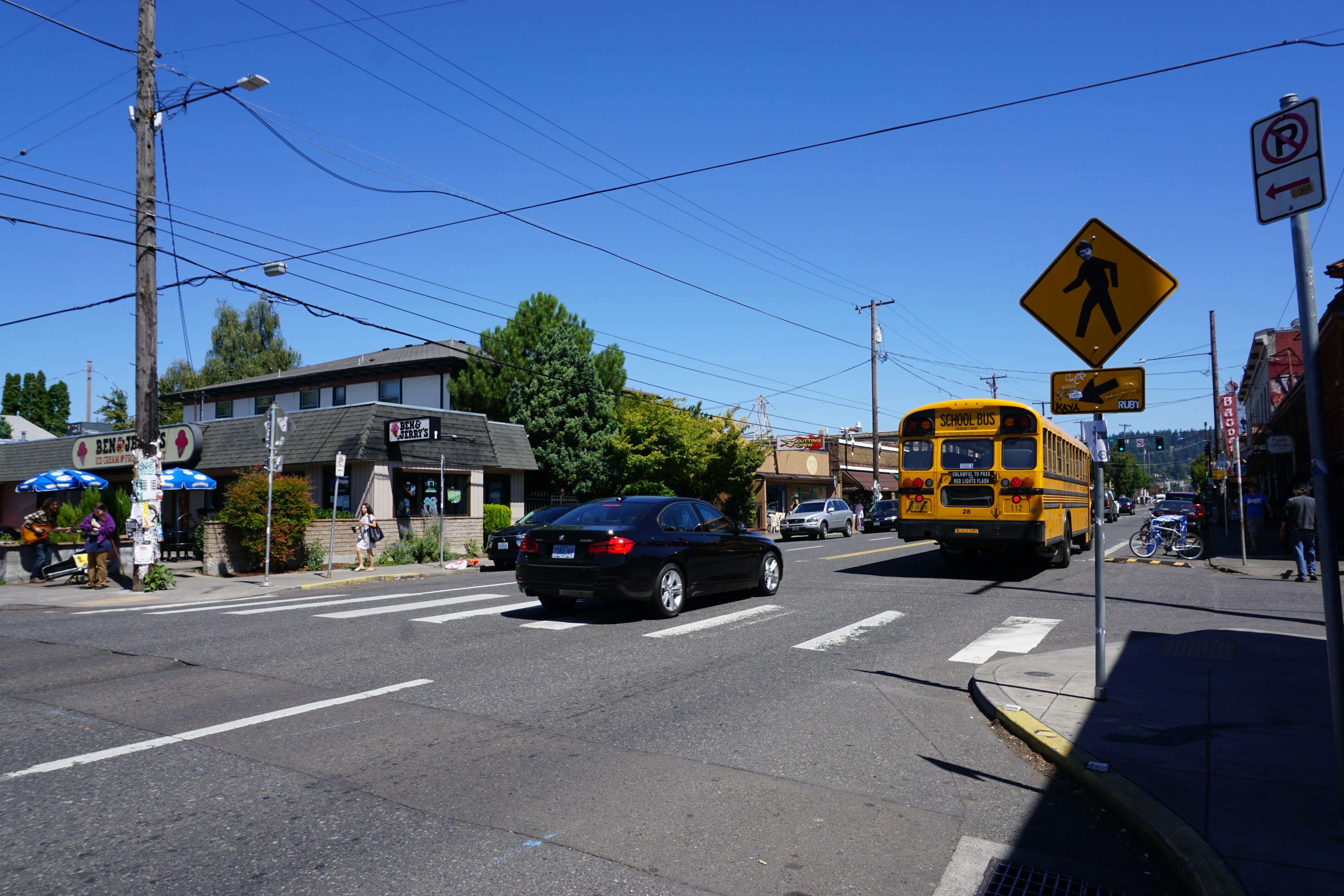 Intersección con un autobús escolar amarillo y un auto negro bajo un cielo azul claro