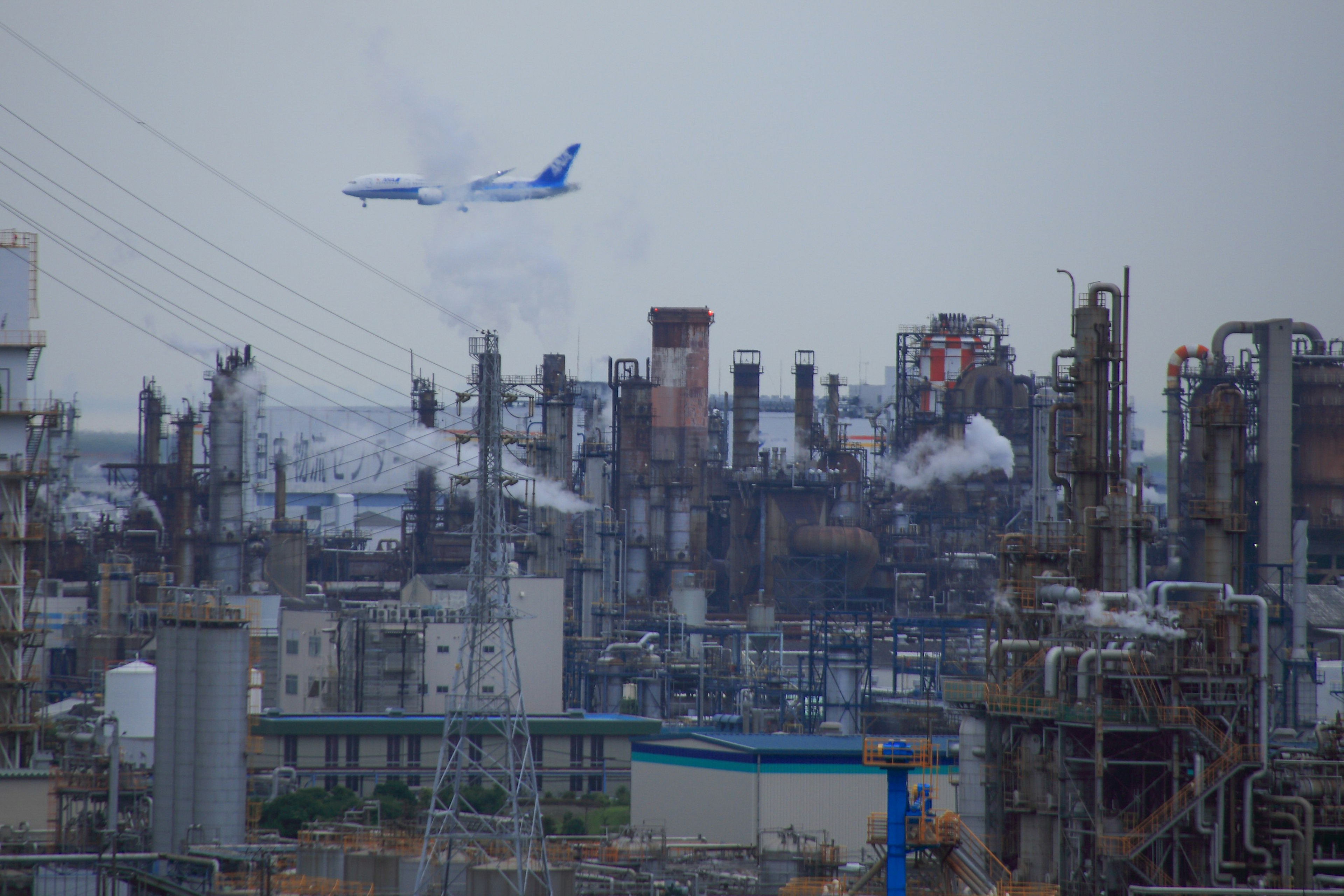 Industrielandschaft mit Rauch und einem Flugzeug am Himmel