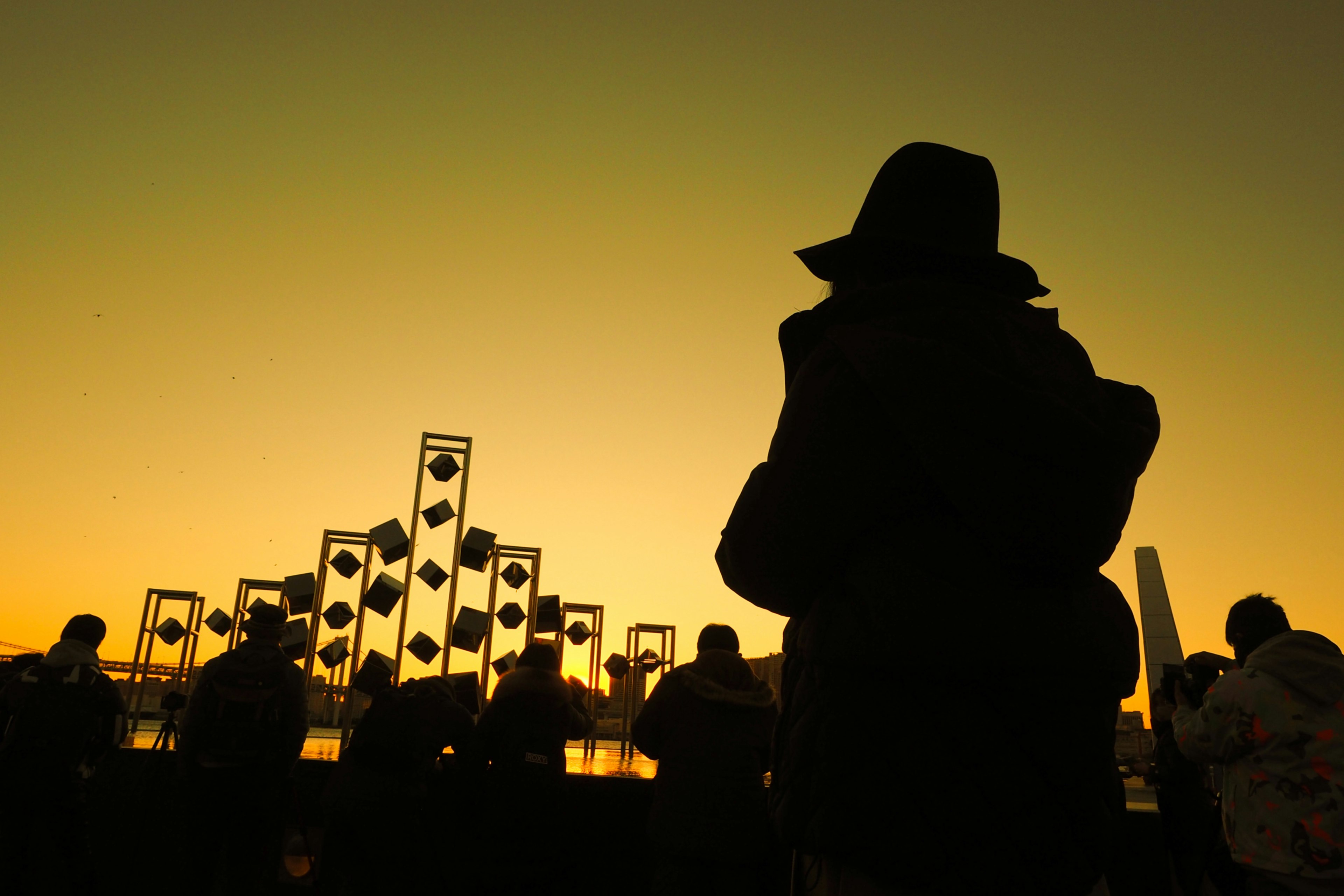 Silhouette di una persona in piedi contro un tramonto con strutture artistiche sullo sfondo