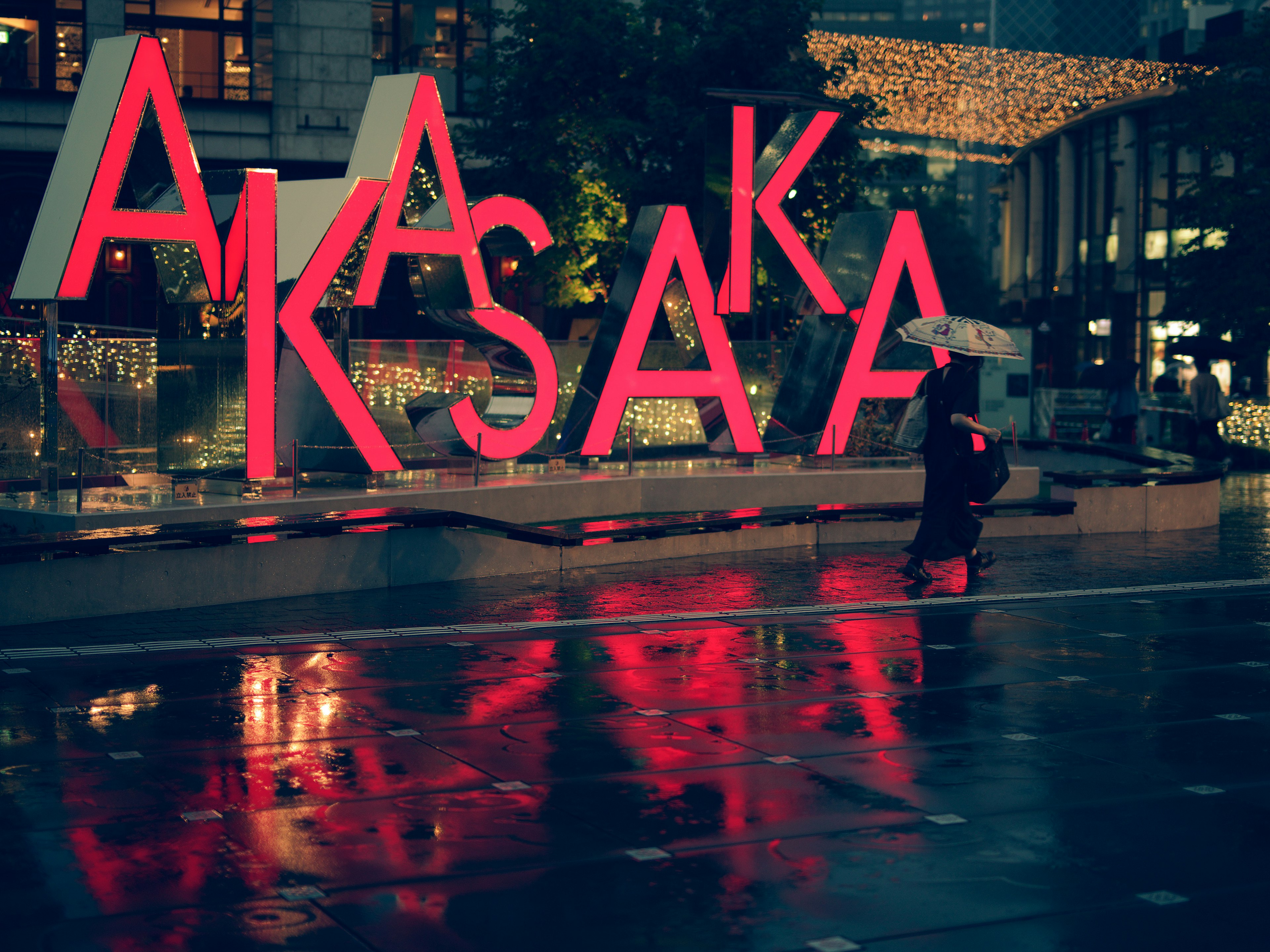 Large pink sign reading AKASAKA with reflections on wet pavement