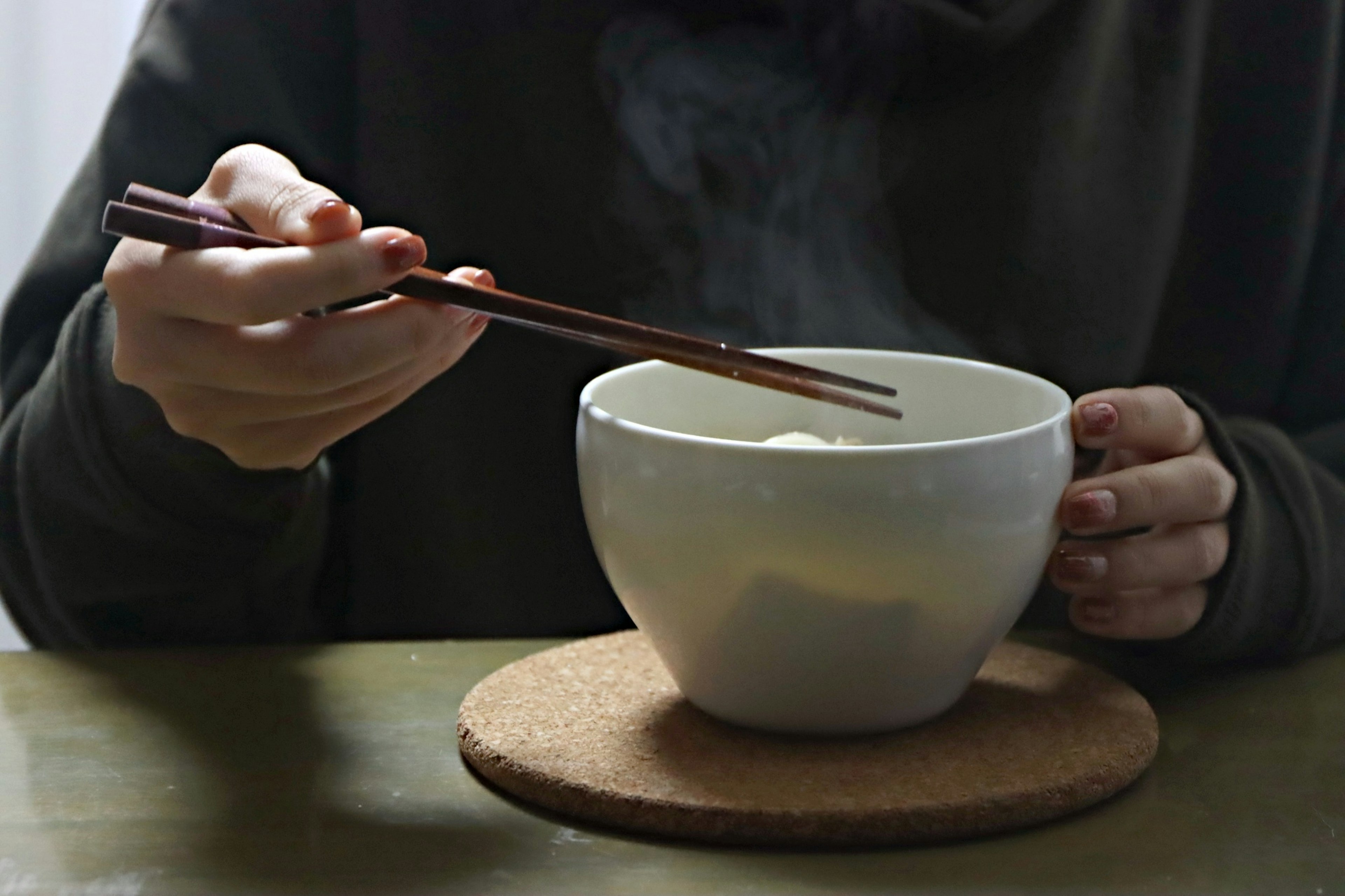 Hand holding a steaming white bowl with chopsticks