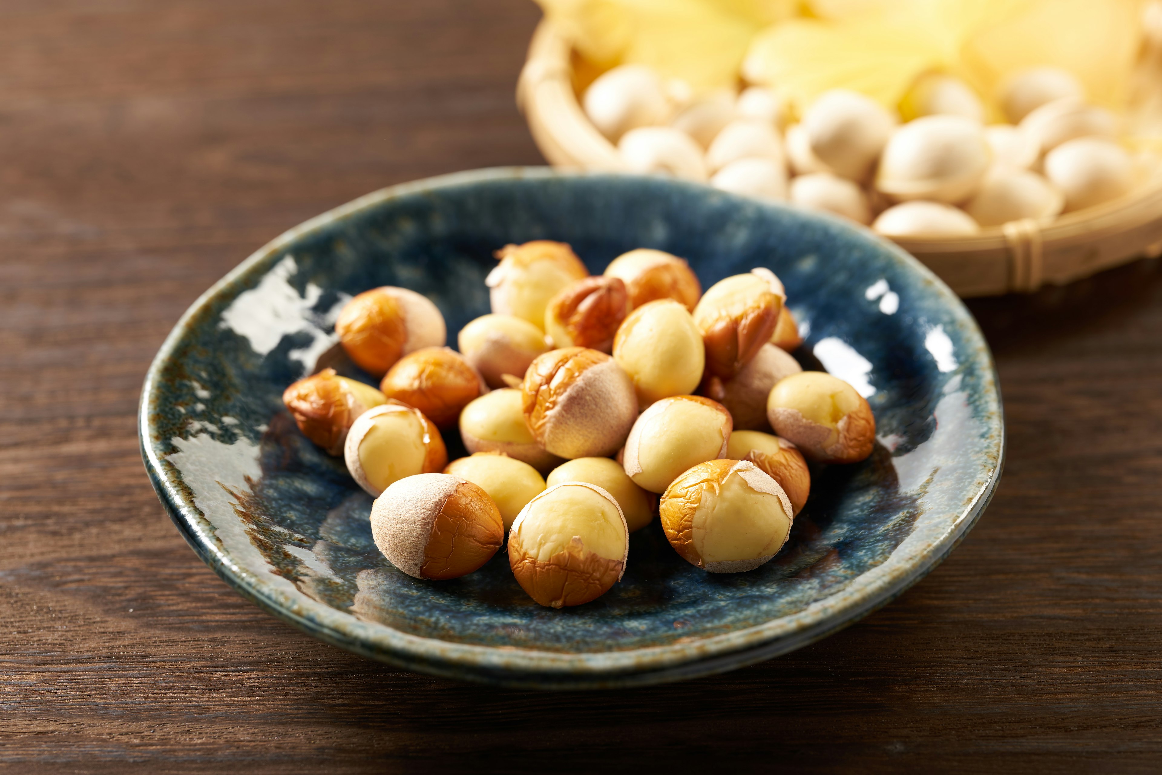 Roasted chestnuts on a blue plate with a basket of chestnuts in the background