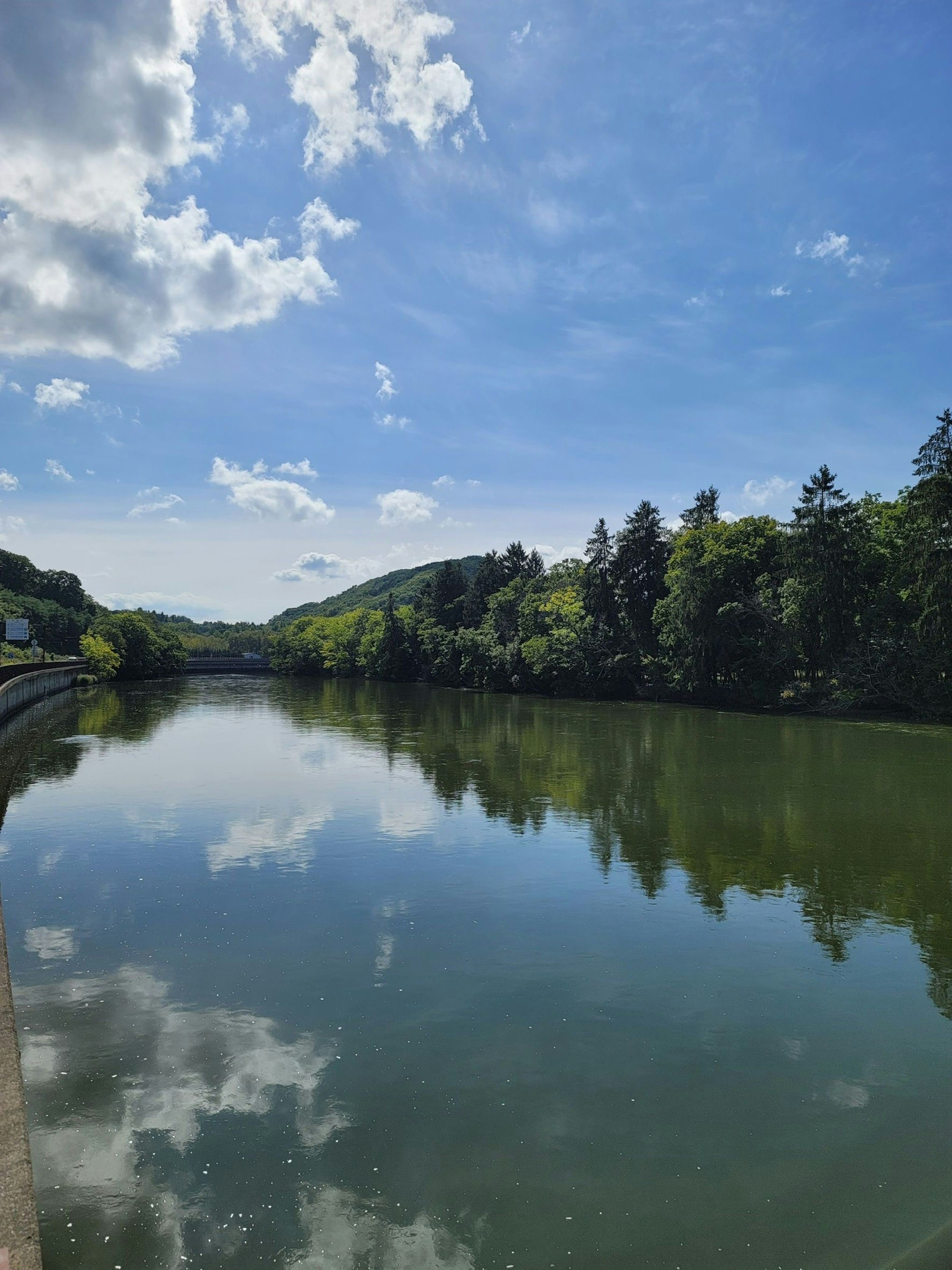 Paisaje sereno de río reflejando el cielo azul y nubes blancas rodeado de exuberante vegetación y colinas