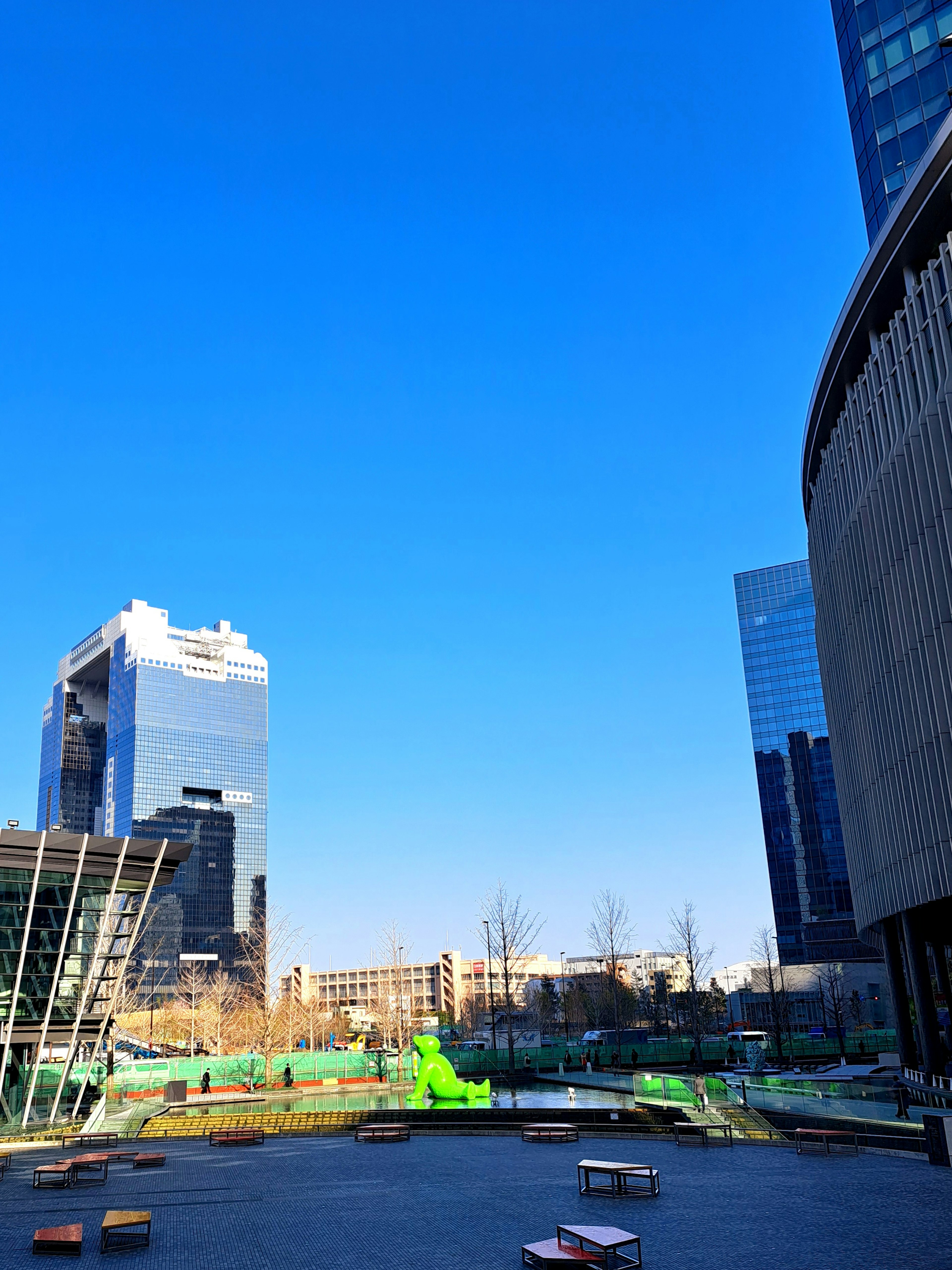 Paysage urbain avec des bâtiments modernes et une sculpture verte sous un ciel bleu clair