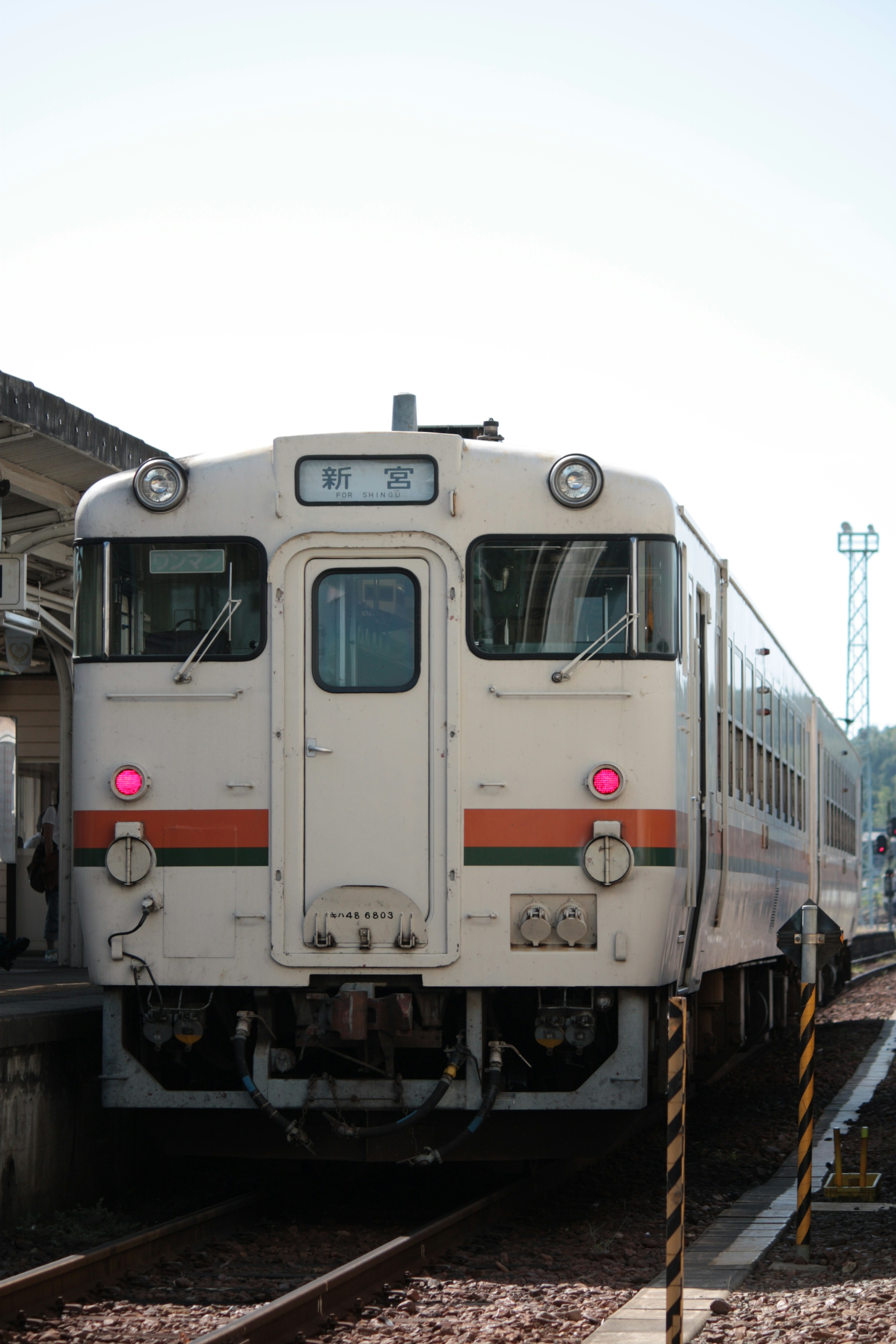 白い色の列車が駅に停車中で前面に赤いライトがある