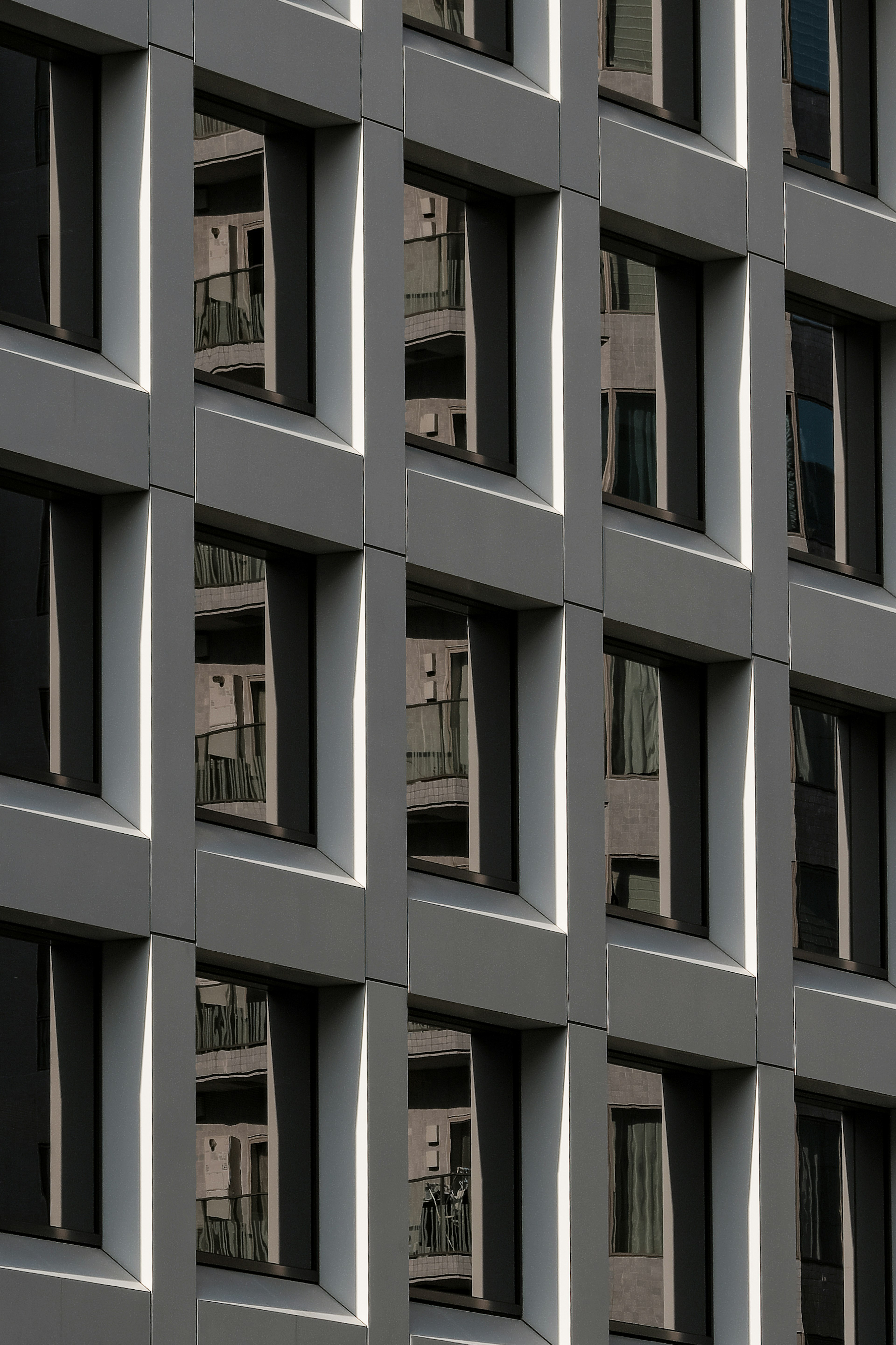 Image d'une façade de bâtiment gris avec des fenêtres rectangulaires distinctives et des reflets