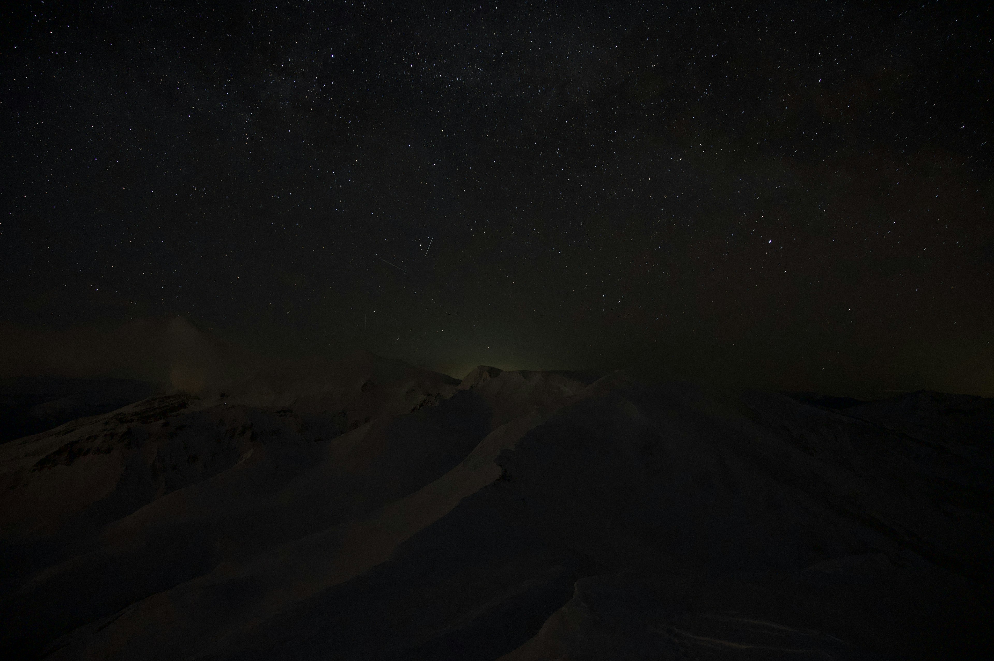 Dark night sky filled with stars over snow-covered mountains