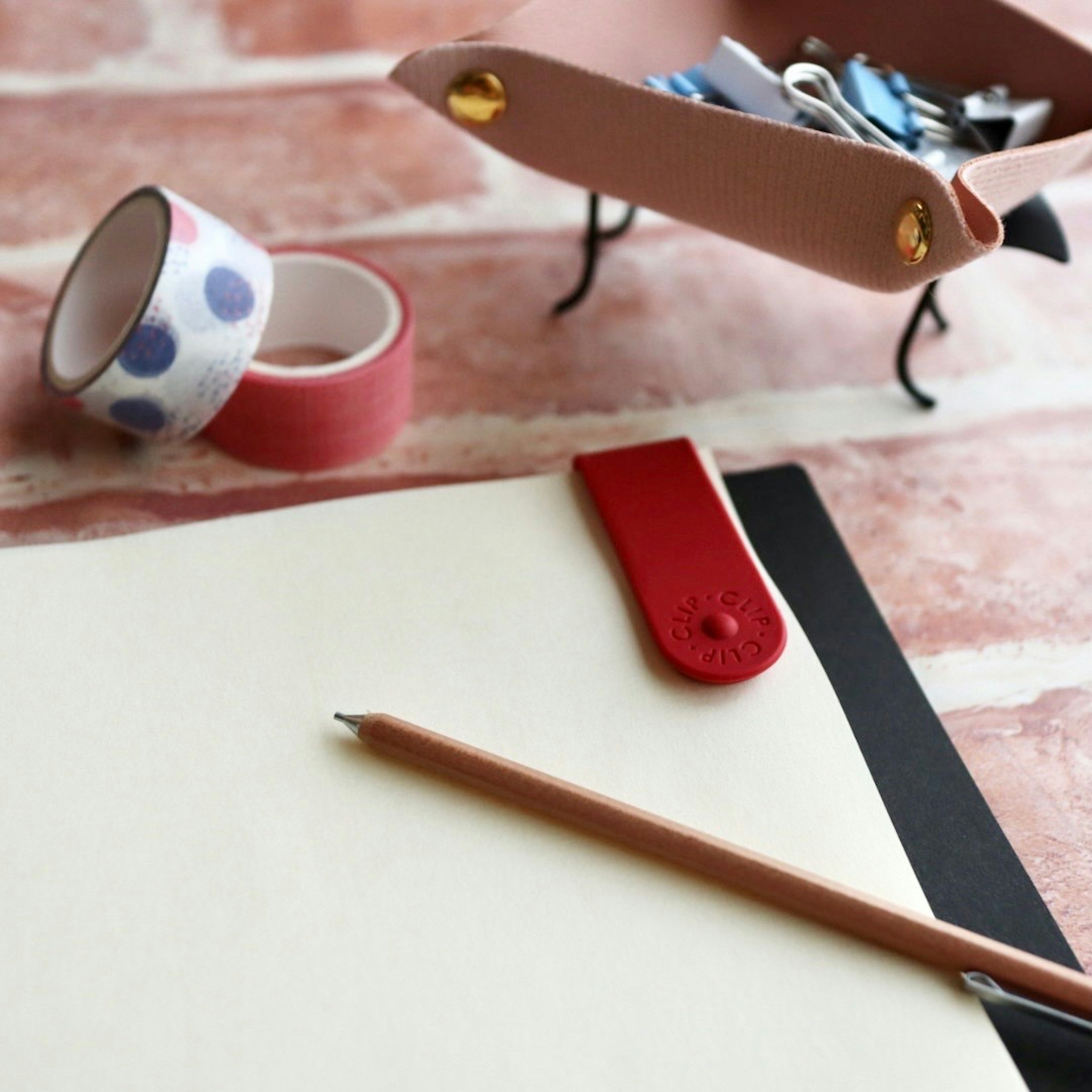 Immagine di cancelleria su una scrivania con un foglio bianco un fermaglio rosso e nastro washi colorato