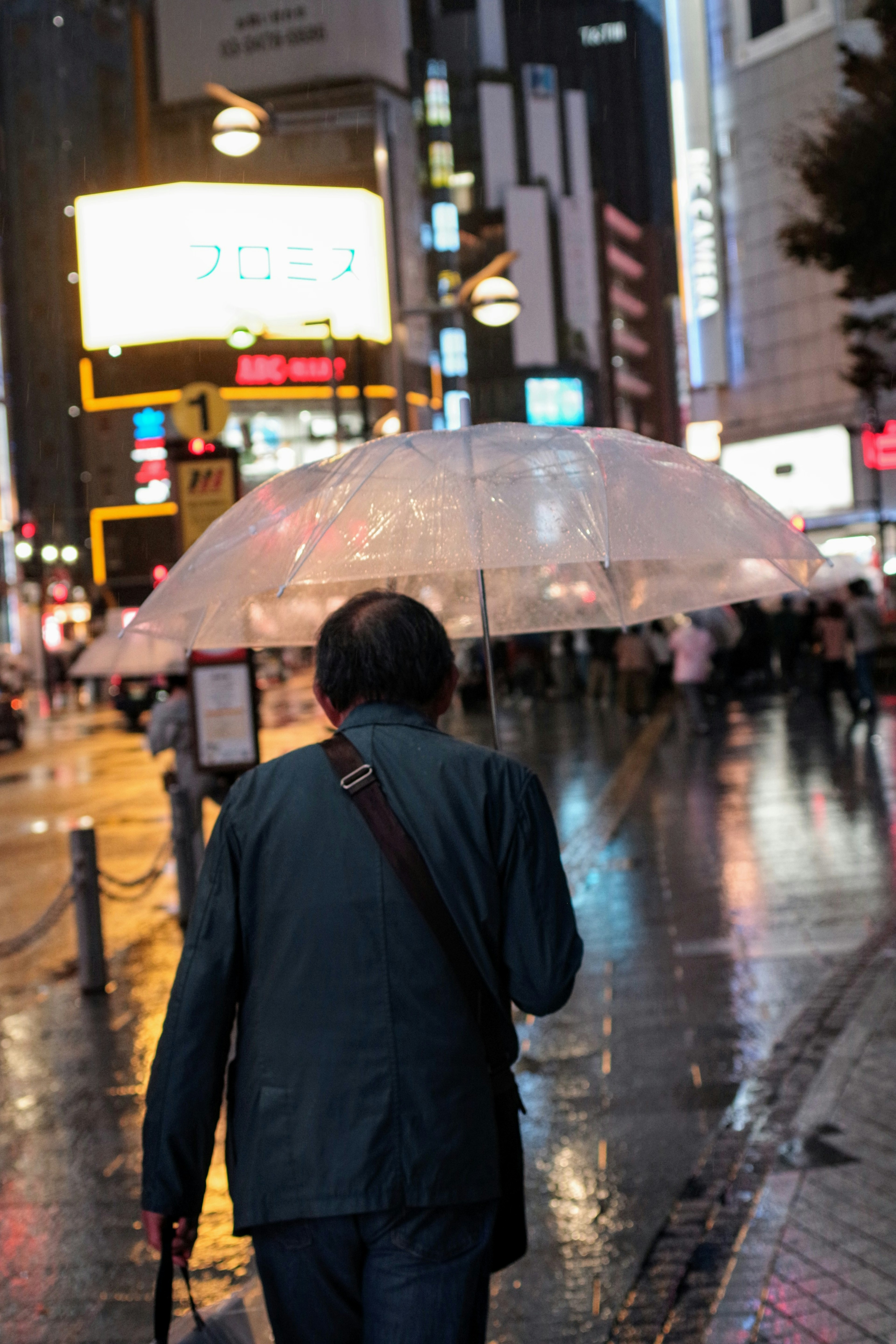 A man walking in the rain holding a transparent umbrella in a city setting